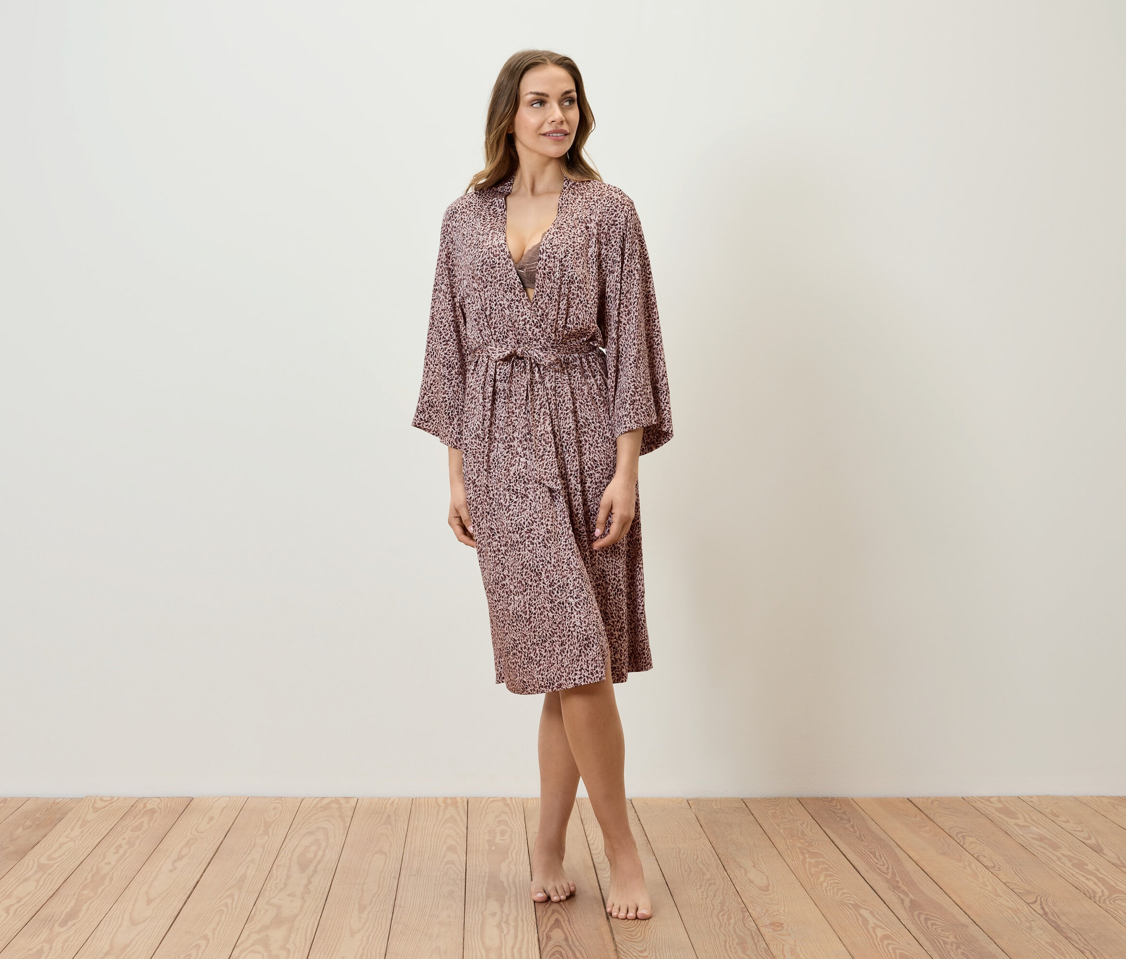 Žena stojí na dřevěné podlaze a má na sobě župan s potiskem.