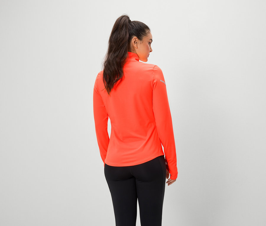 Žena zády k fotoaparátu má na sobě oranžový top s dlouhým rukávem a černé legíny.