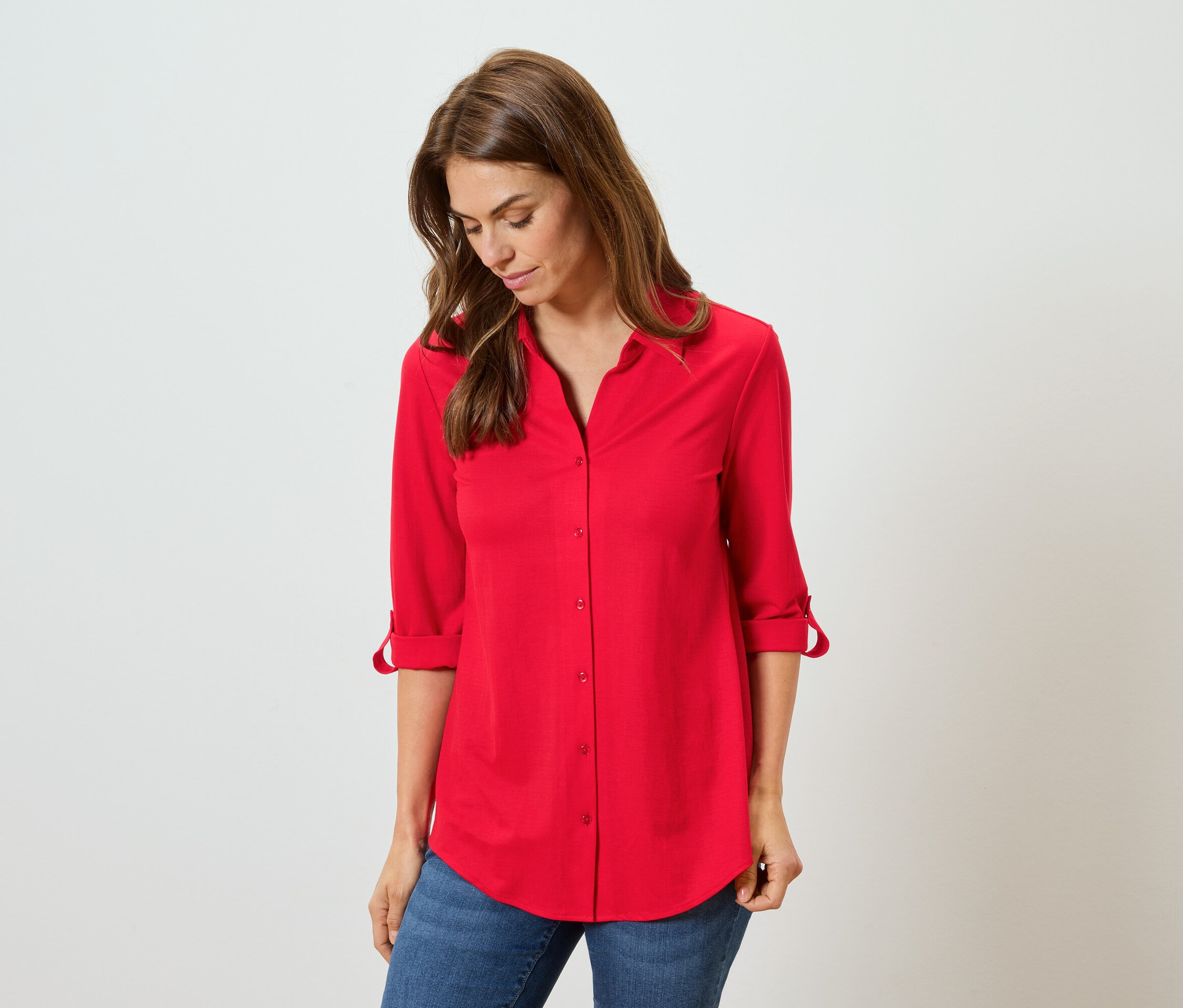 Žena má na sobě červenou košili a modré džíny.