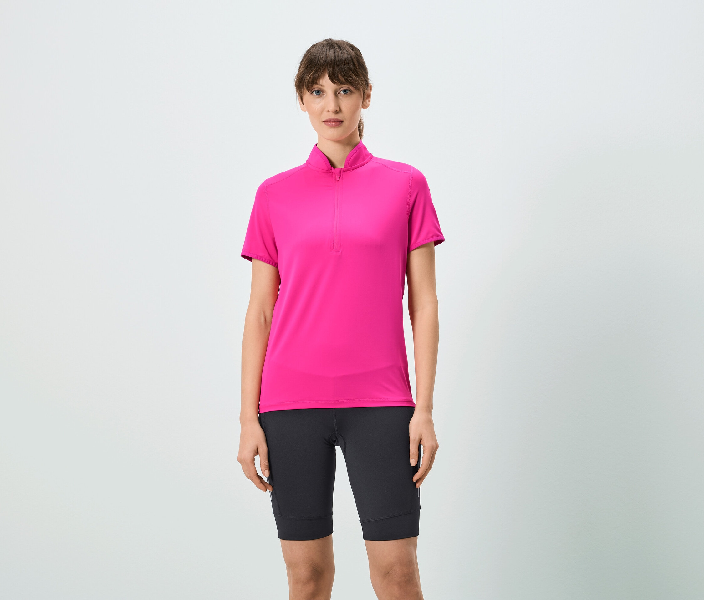Žena má na sobě růžové tričko s krátkým zipem a černé šortky.