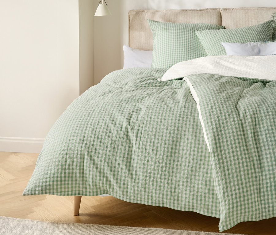 Postel se světle zelenobílou kostkovanou přikrývkou a odpovídajícími polštáři.