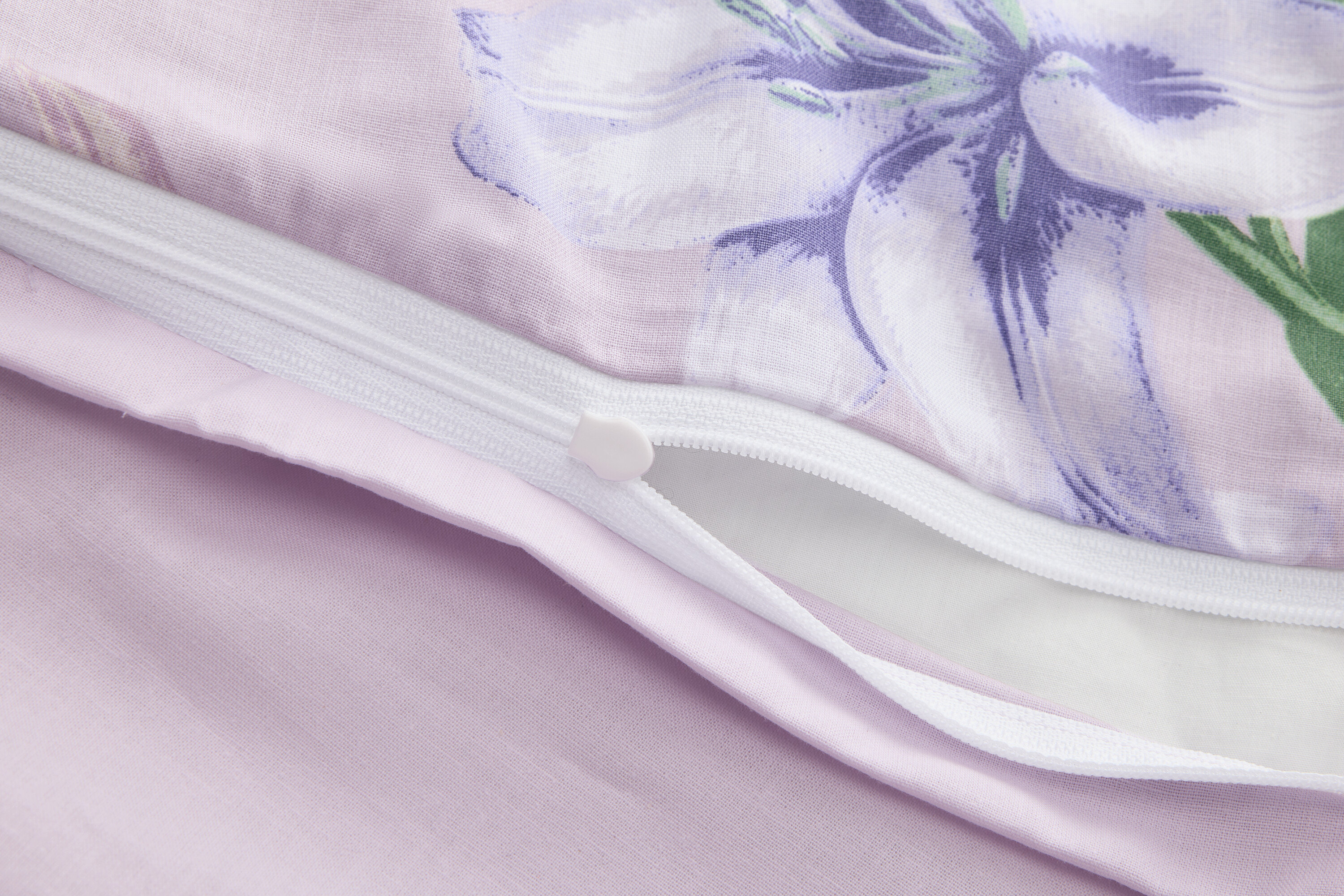 Detailní záběr na částečně otevřený fialový povlak na přikrývku s květinovým potiskem a zipem.