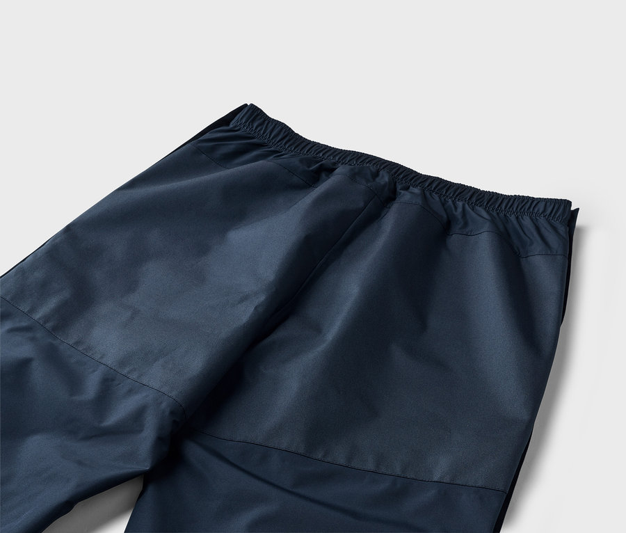 Detailní záběr na zadní stranu tmavě modrých kalhot s elastickým pasem na bílém pozadí.