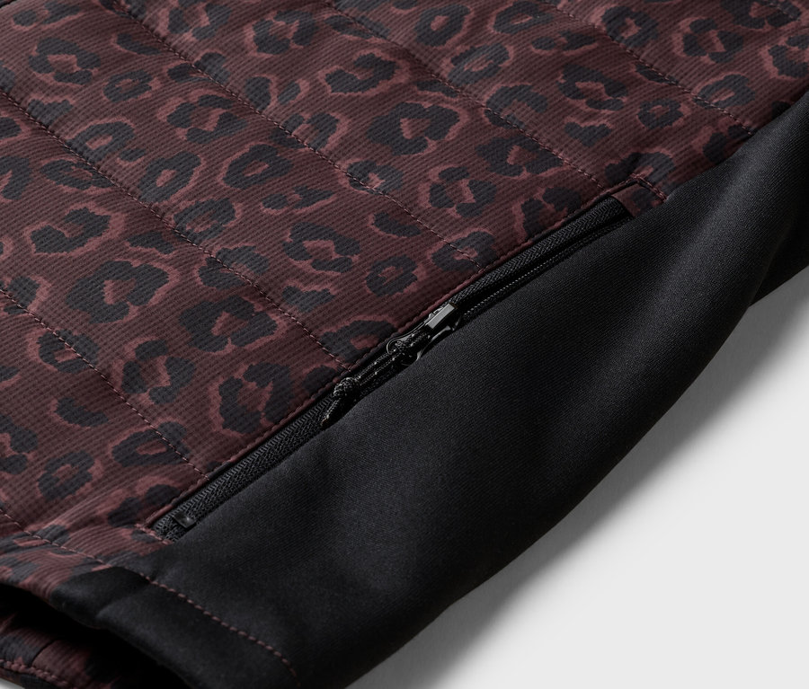 Detailní záběr prošívané bundy s leopardím vzorem a částečně otevřeným zipem na boku.