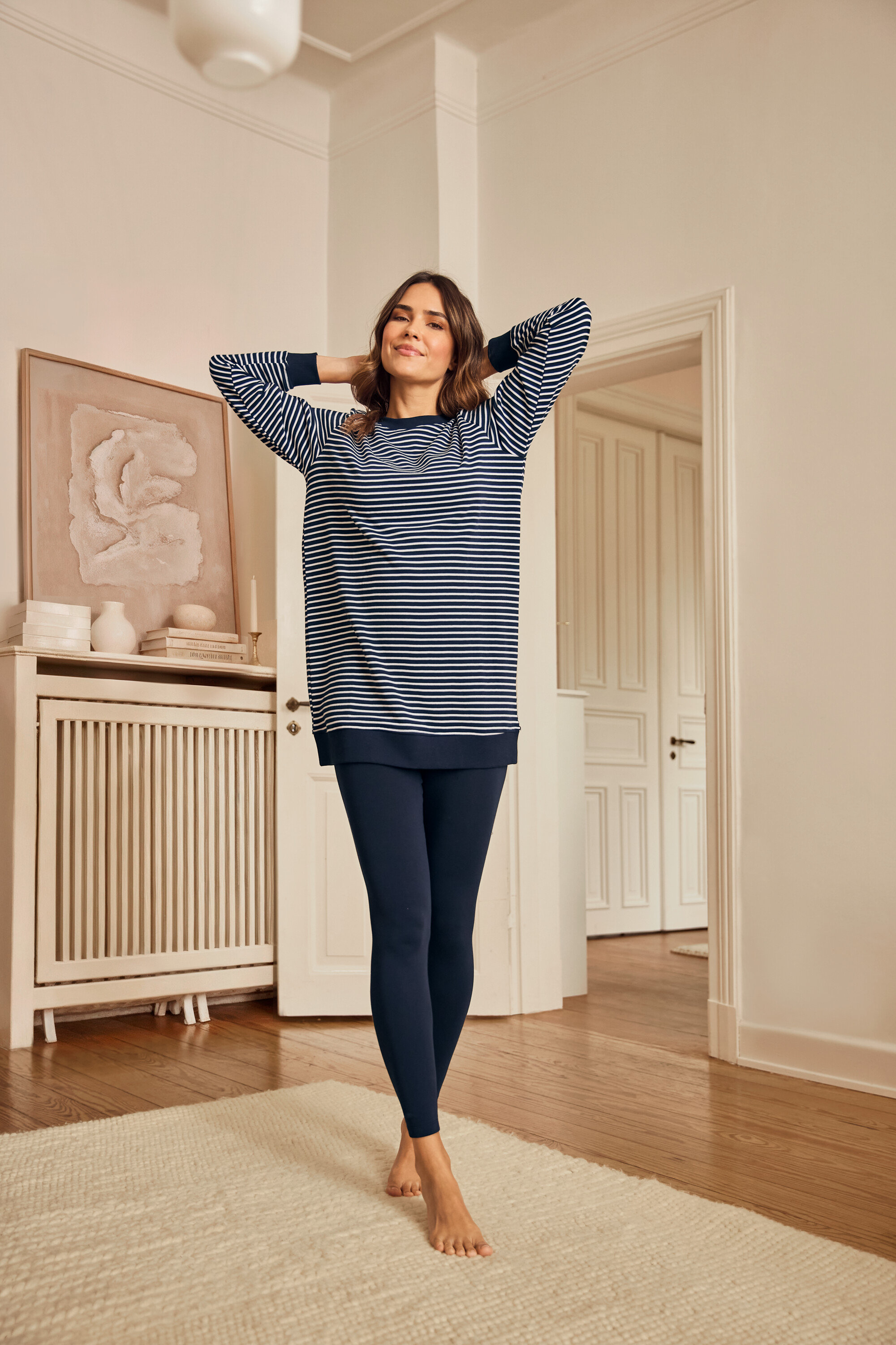 Žena v pyžamu s legínami stojí bosa na koberci.