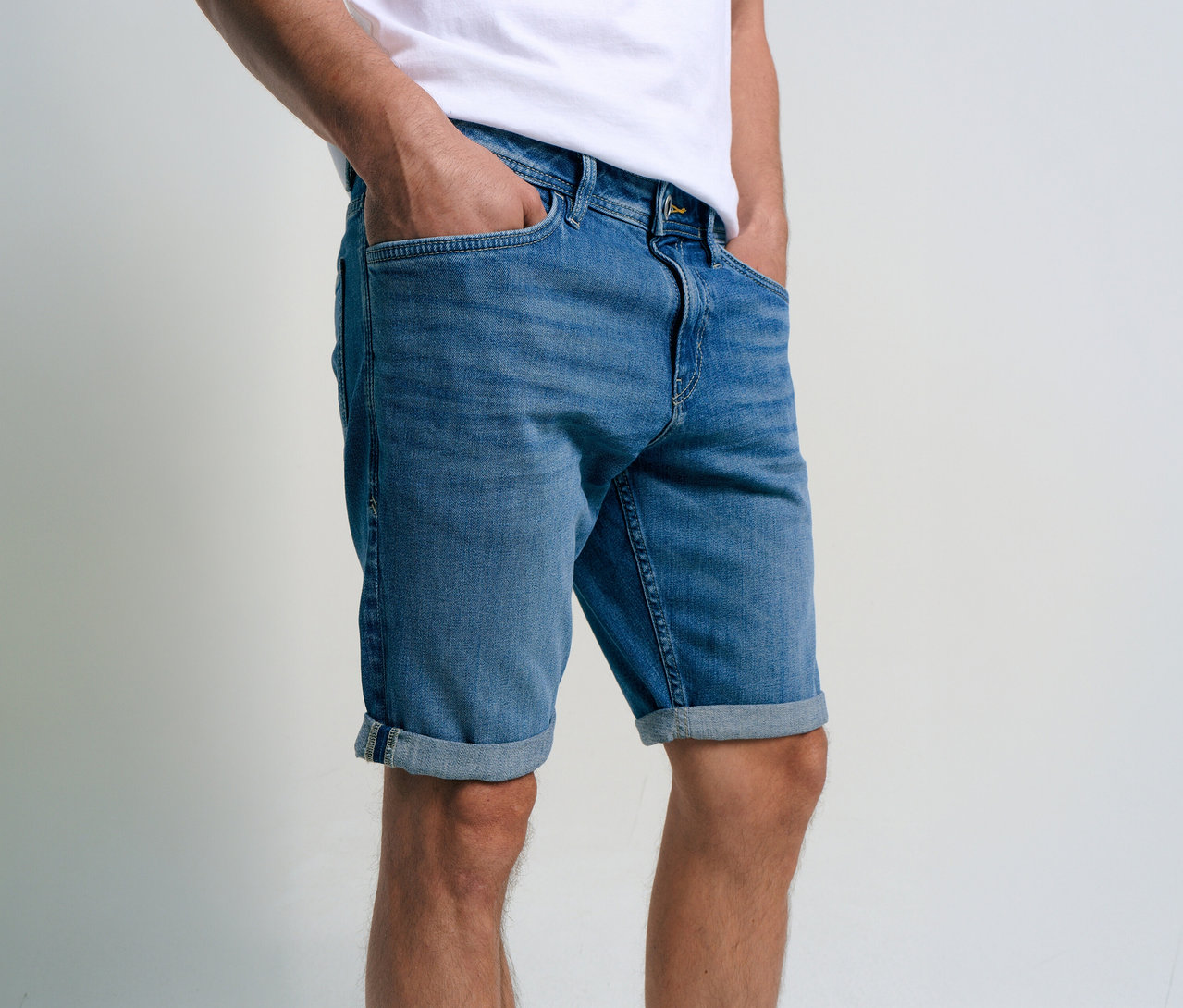 Muž má na sobě džínové šortky Tom Tailor TTJOSH REGULAR SLIM, mid stone bright blue denim, s rukama v kapsách.