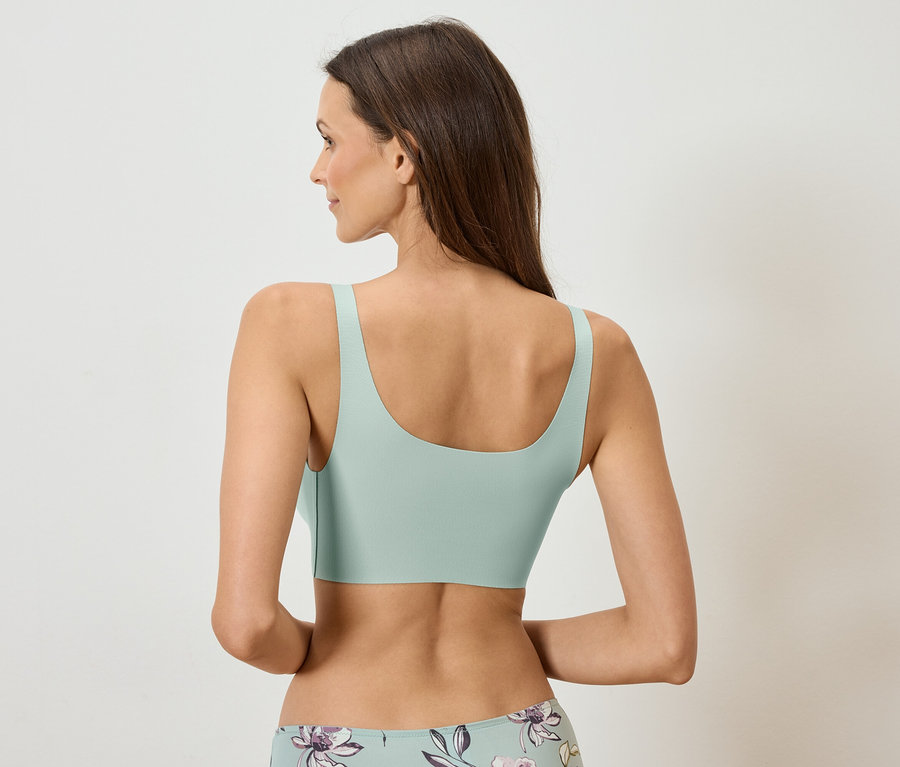 Pohled zezadu na ženu s dlouhými hnědými vlasy, oblečenou v mátové podprsence a květinových kalhotkách.