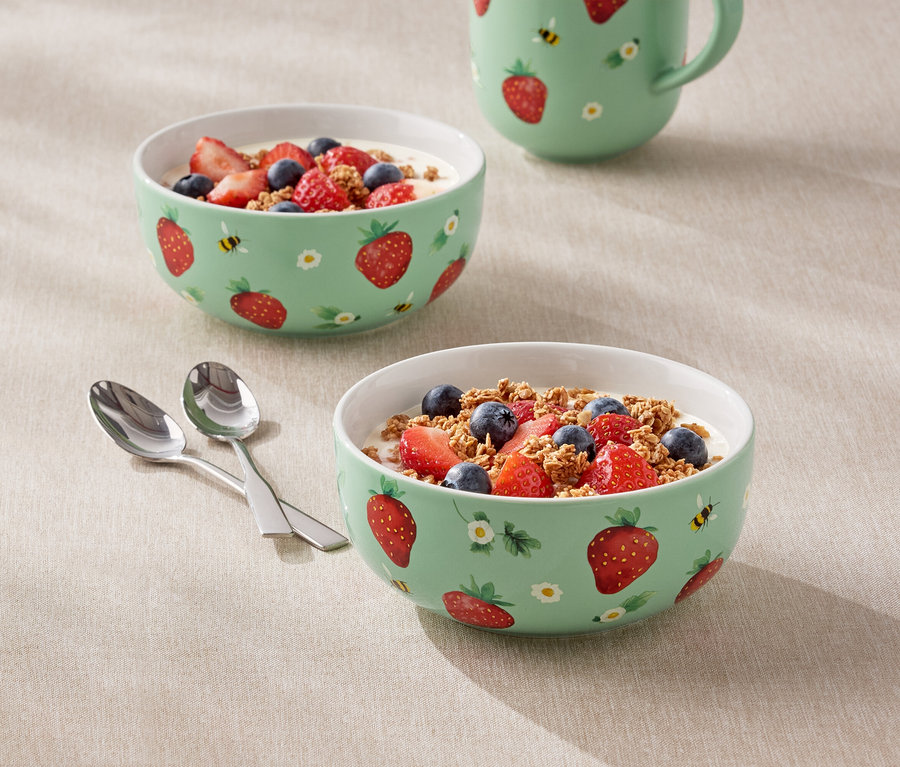 Dvě mísy naplněné jogurtem, jahodami a borůvkami se vzorem jahod a džbán stojí na stole.