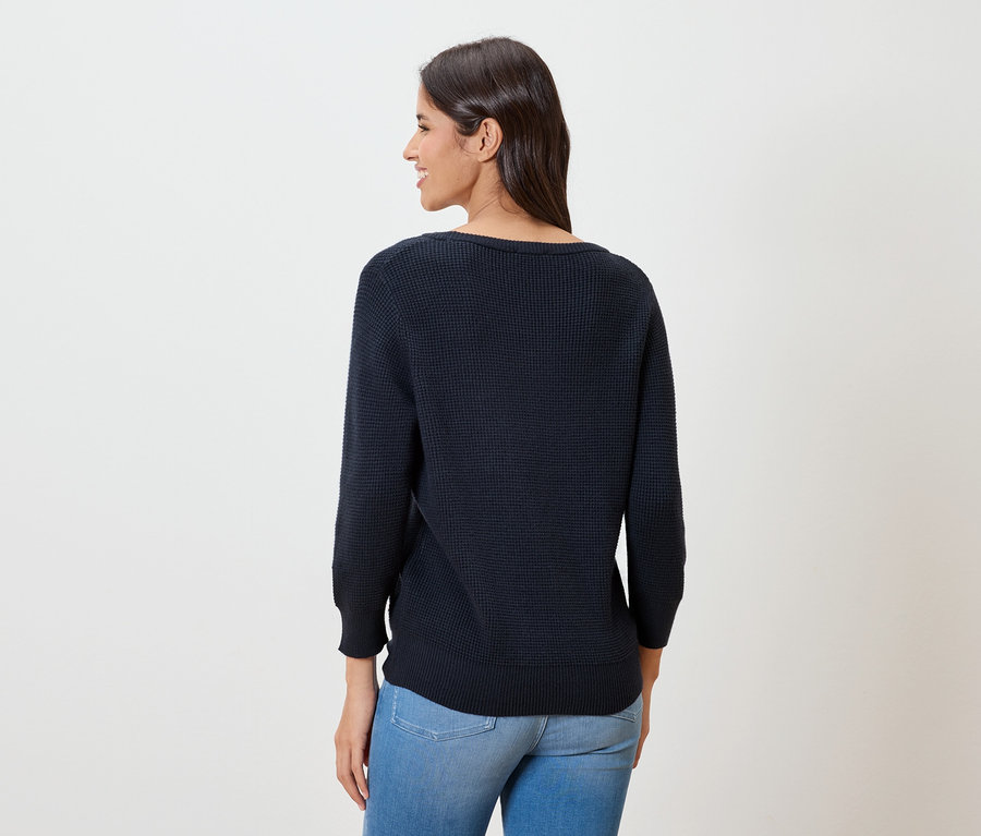 Žena zezadu, má na sobě tmavě modrý tenký svetr a džíny.