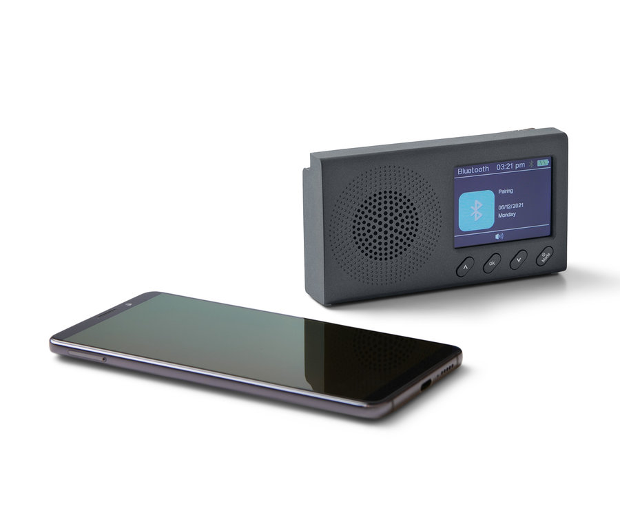 Černé přenosné rádio DAB/FM s Bluetooth a černý smartphone leží na bílém pozadí.
