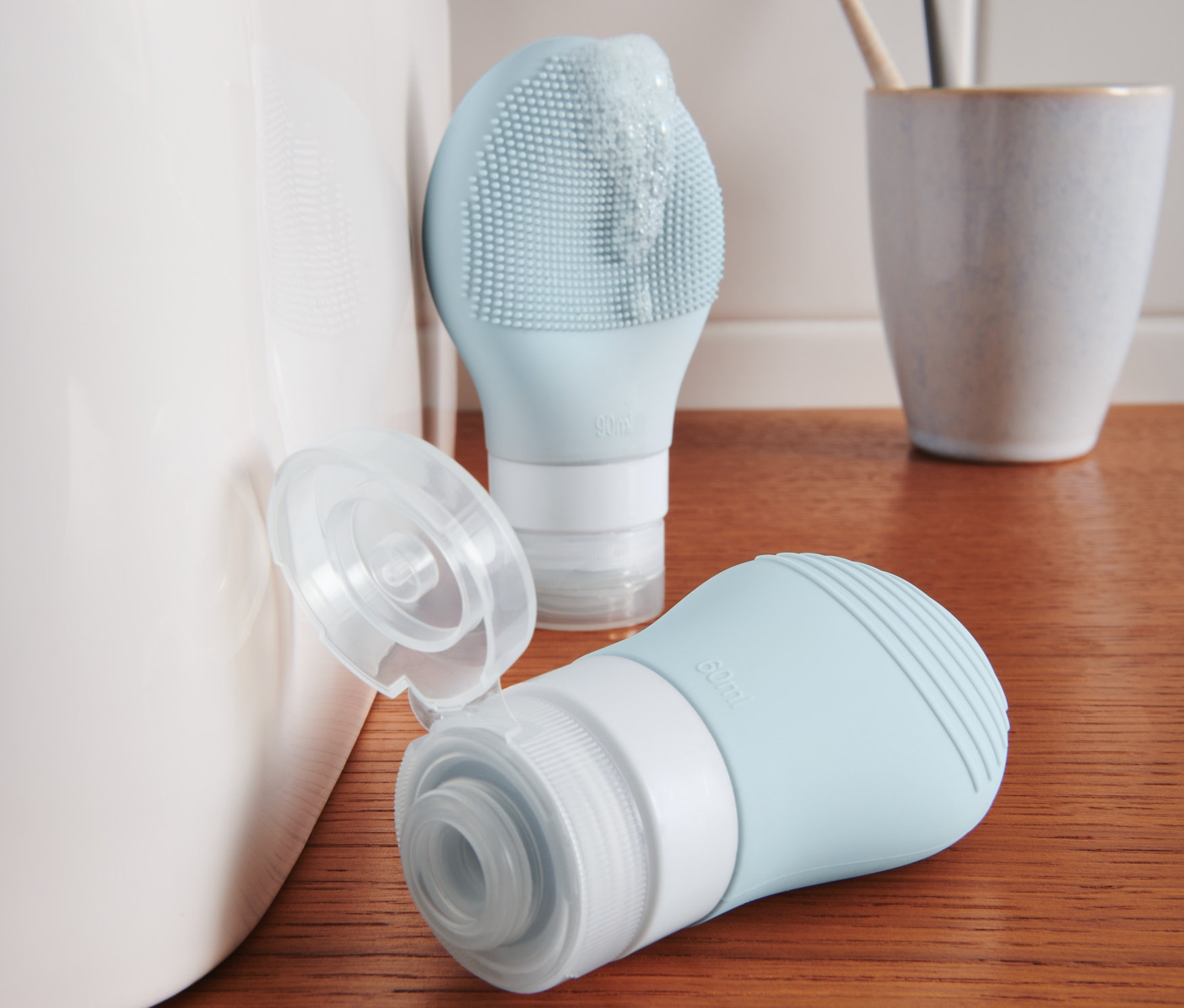 Dvě modré lahvičky na šampon stojí na dřevěné polici vedle umyvadla.