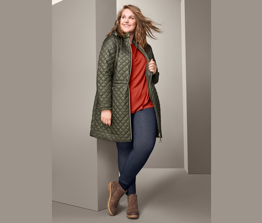 Žena pózuje v prošívaném kabátu s kapucí, tričku oversized, legínách v džínovém vzhledu s podšívkou a v botách z velurové kůže.