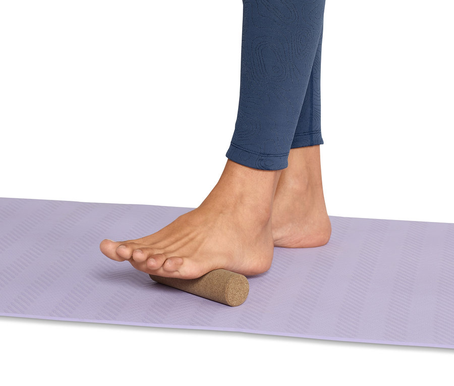 Noha stojí na korkovém mini masážním válečku na fscie na fialové podložce.