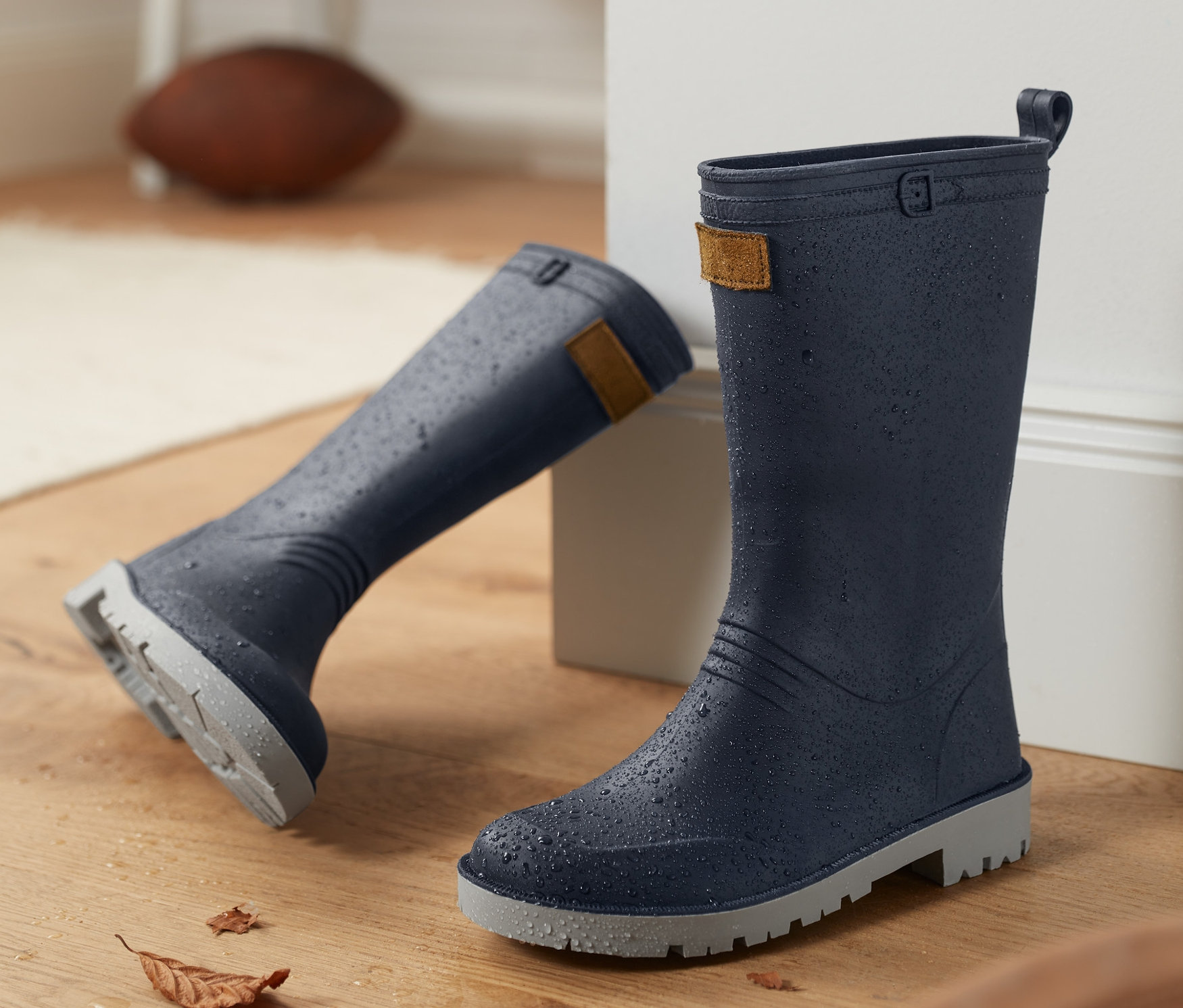 Dvoje modré gumové holínky stojí na dřevěné podlaze.