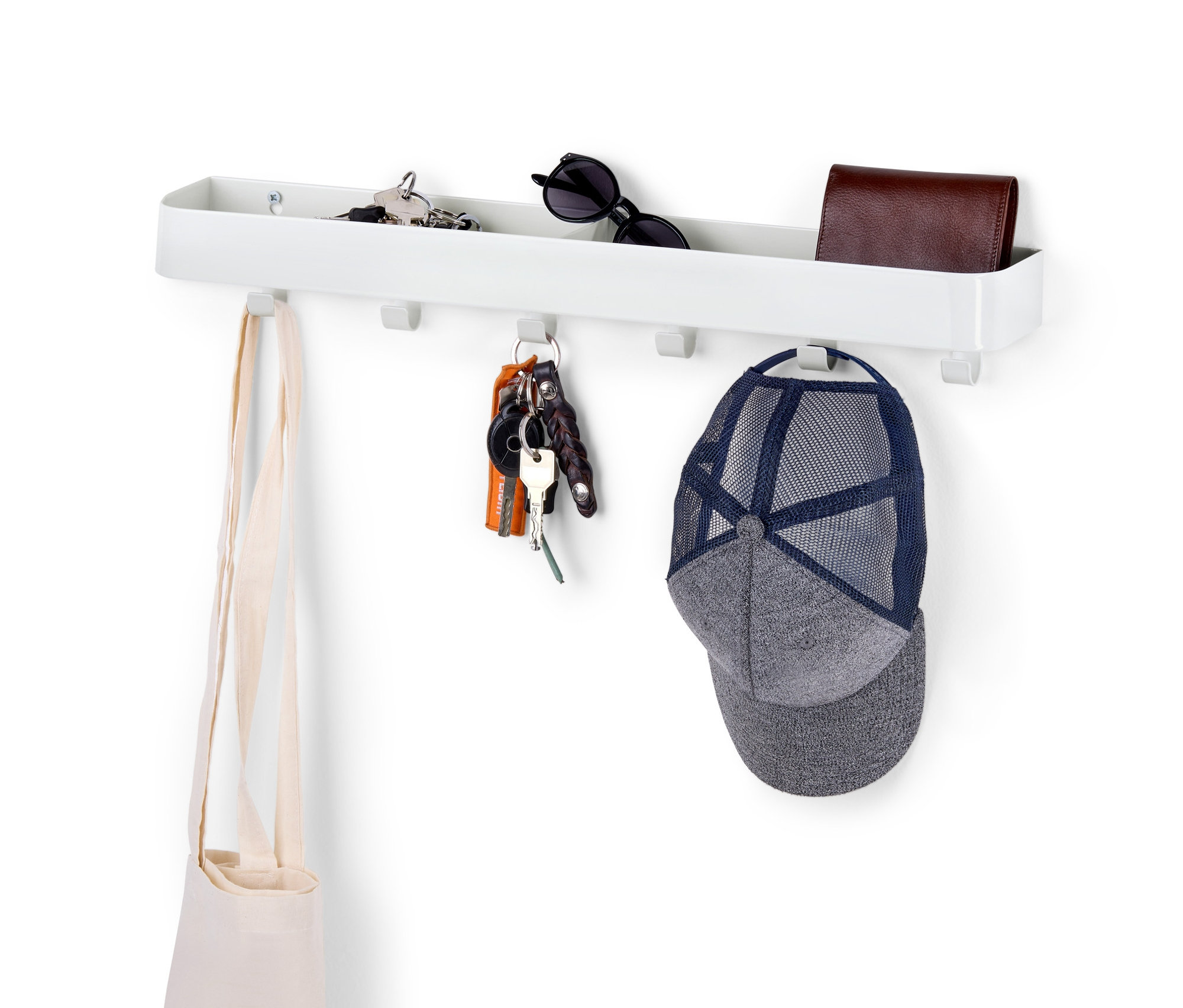 Bílý věšák na klíče s odkládací plochou, na kterém visí klíče, taška a kšiltovka.