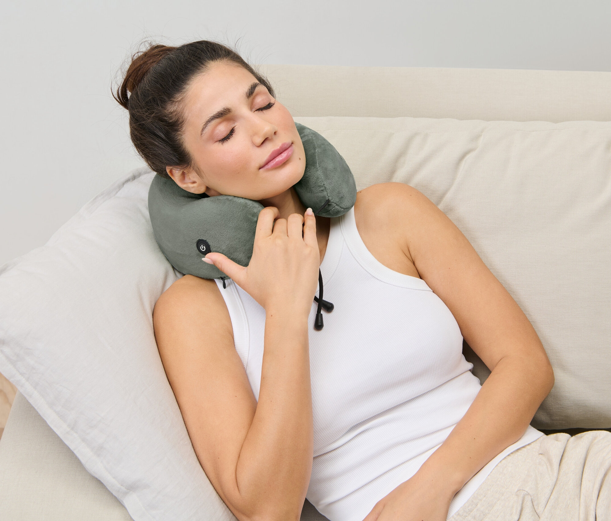 Žena leží na gauči s vibrační masážní poduškou na krk.