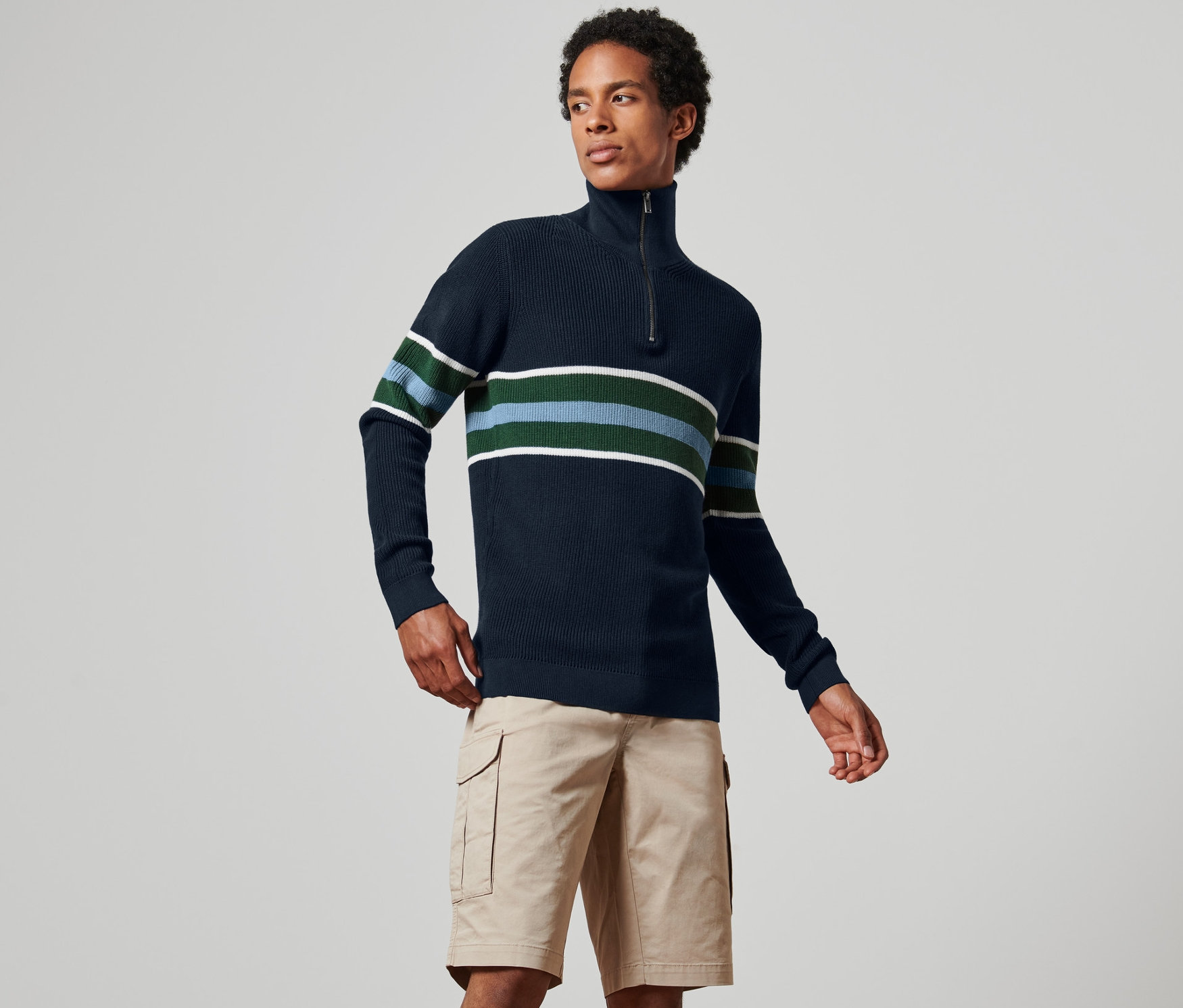 Muž má na sobě tmavě modrý svetr troyer s pruhy a khaki šortky.