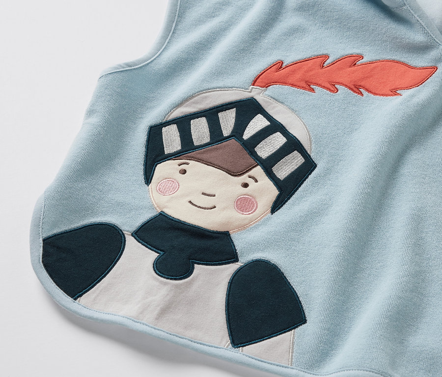 Detail modrého froté ponča s nášivkou rytíře.