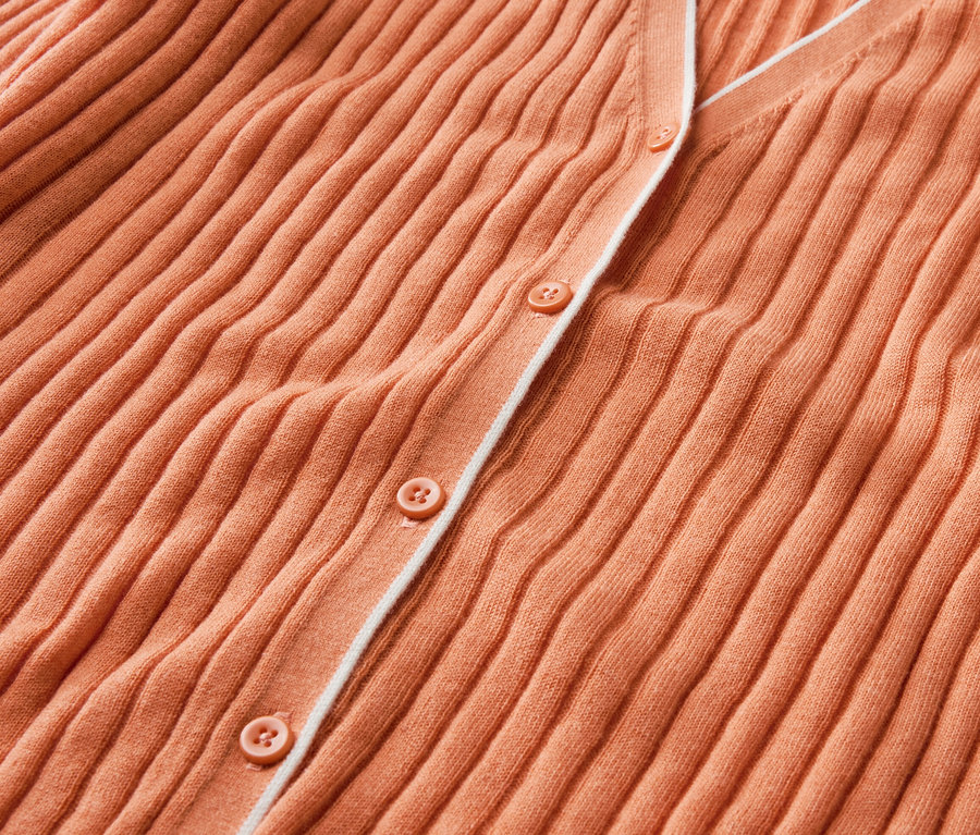 Detailní záběr na oranžový svetr s knoflíky a hedvábím.