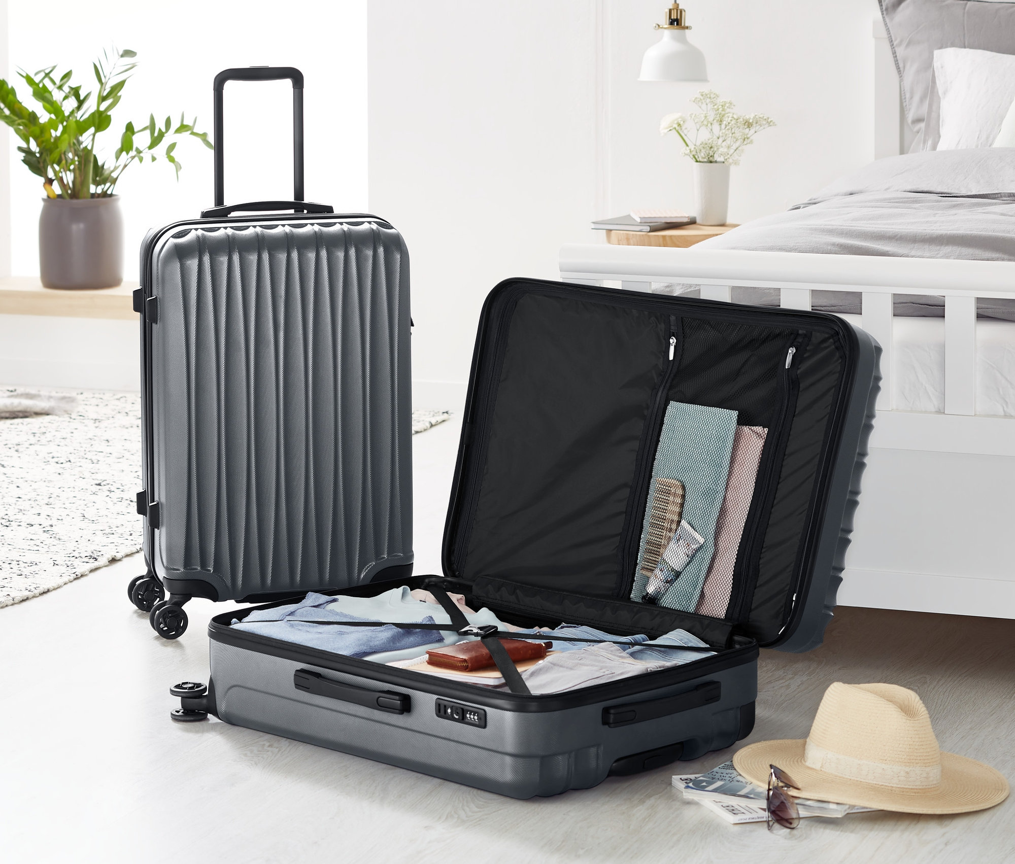 Dva šedé kufry z tvrdé skořepiny, střední a velký, stojí na podlaze, jeden otevřený.