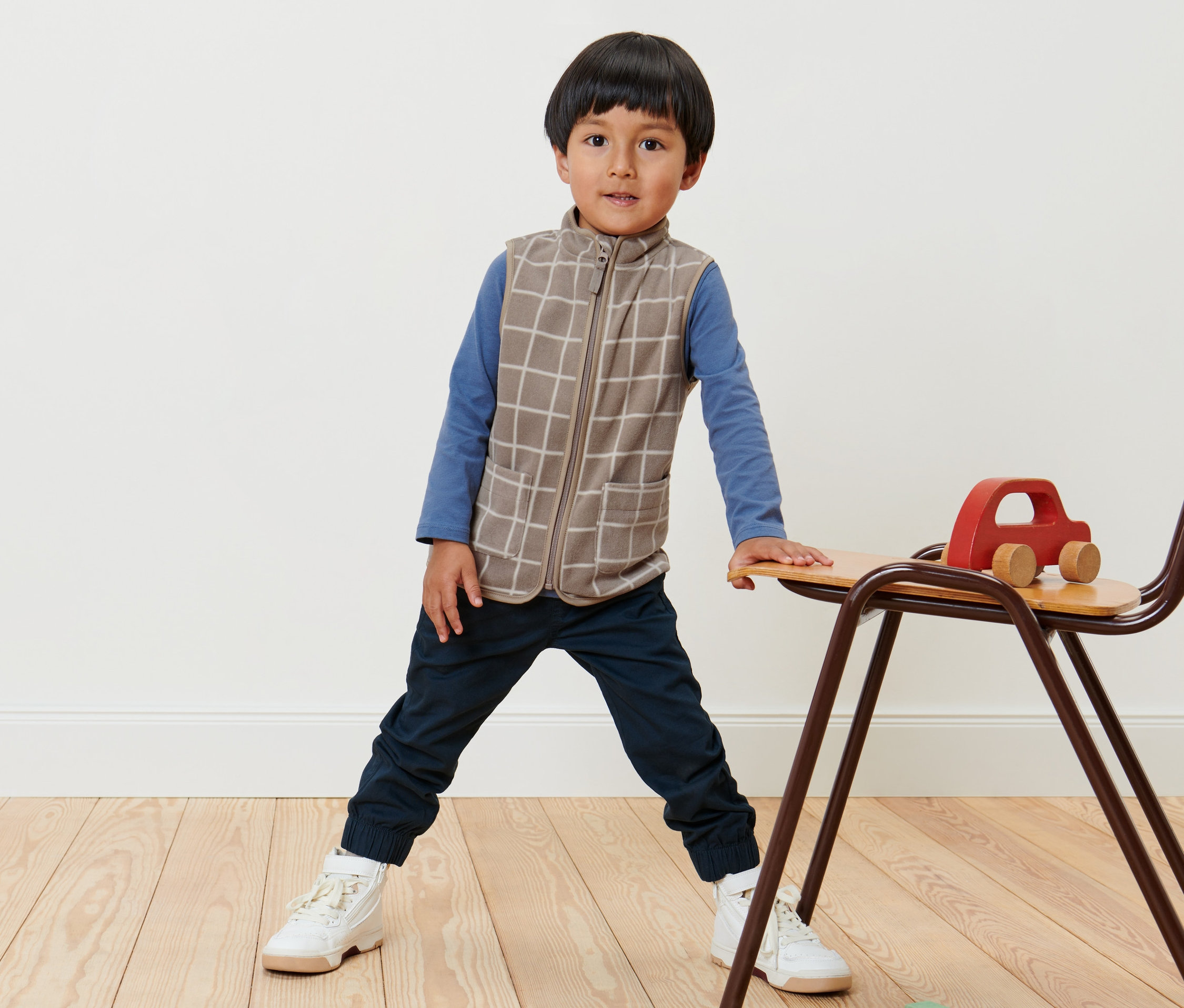 Chlapec stojí a má na sobě dětskou fleecovou vestu s károvaným vzorem.