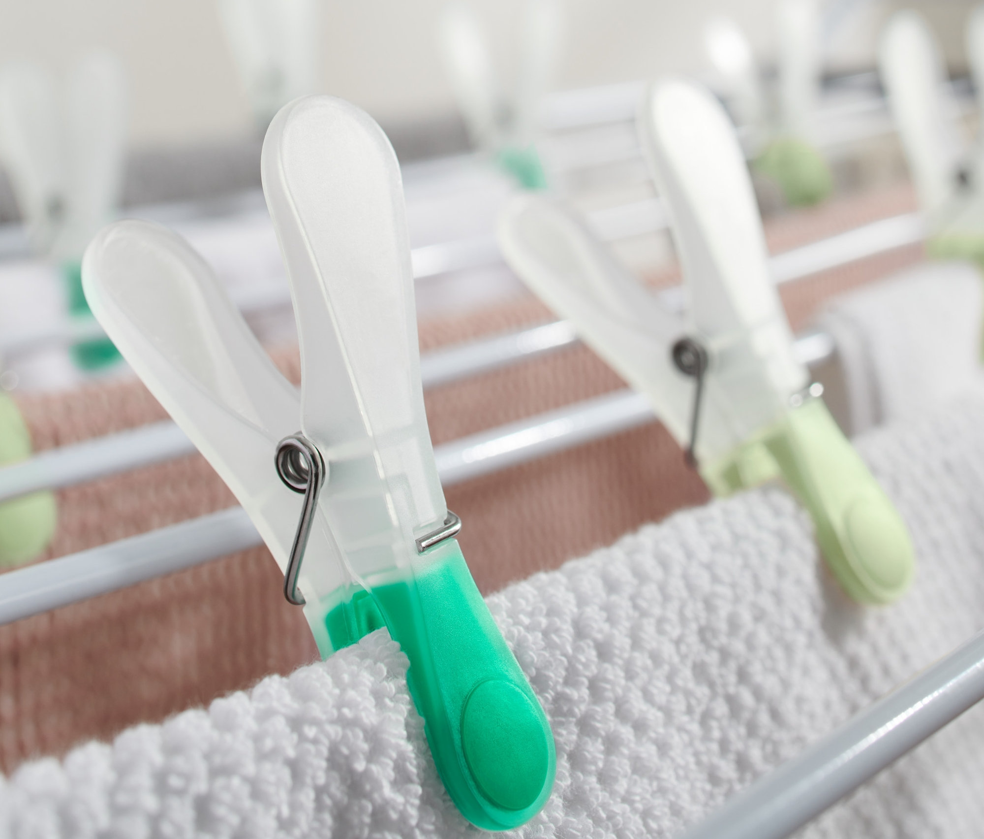 Detailní záběr na 20 kolíčků na prádlo, které drží bílé a růžové ručníky na sušáku.