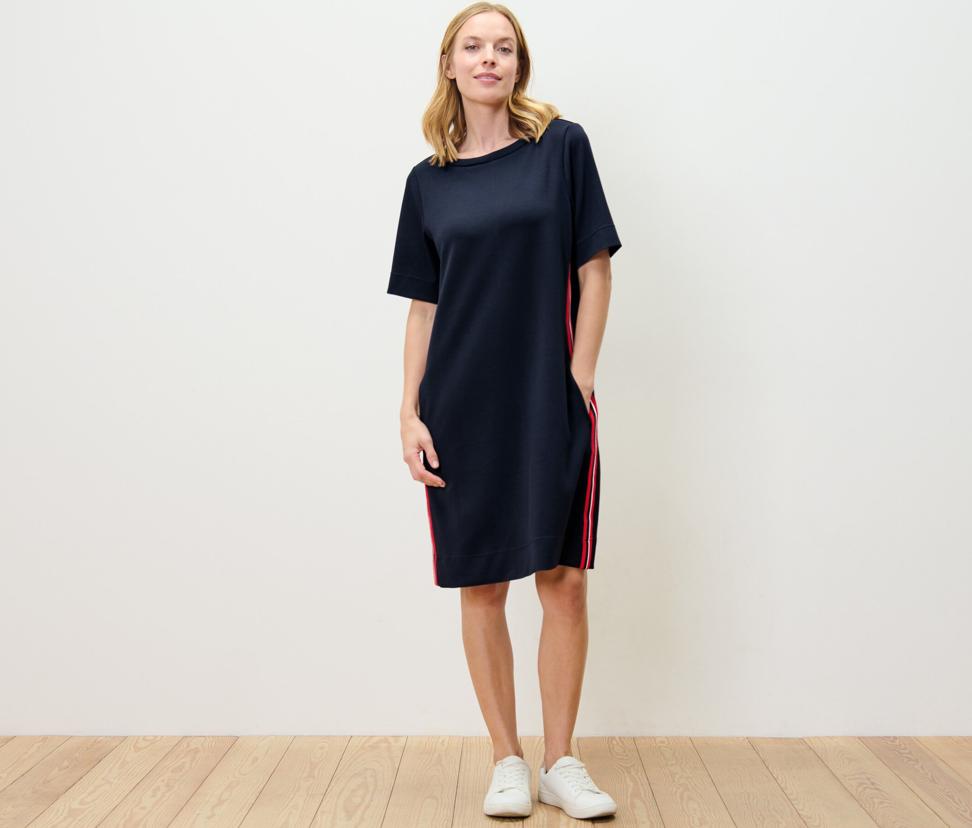 Žena stojí a má na sobě teplákové šaty s galonovými pruhy.