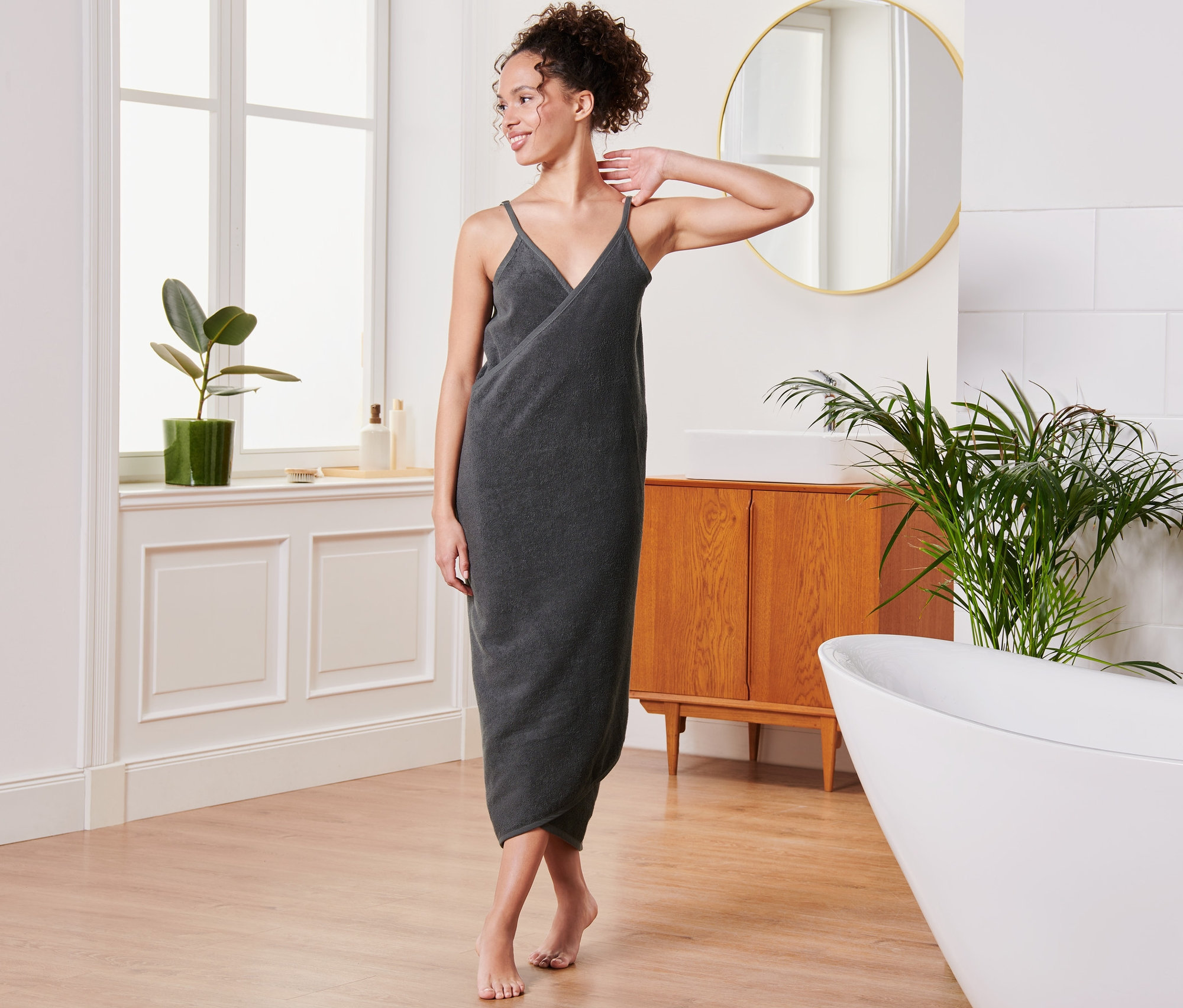 Žena pózuje v koupelně v antracitových ručníkových šatech.