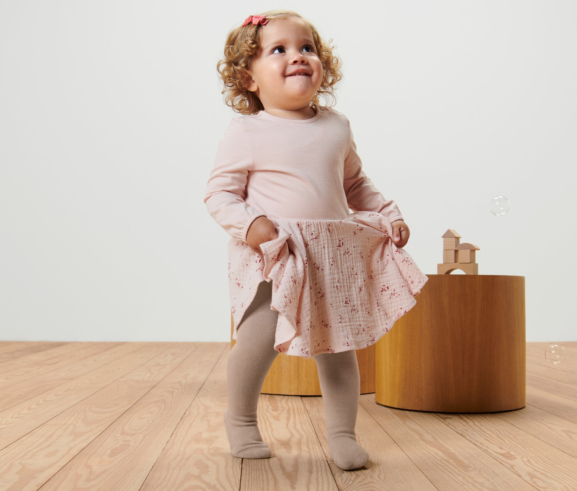 Holčička v růžových šatech a béžových punčocháčích (Dětské punčocháče, 5 ks) si hraje s bublinami.