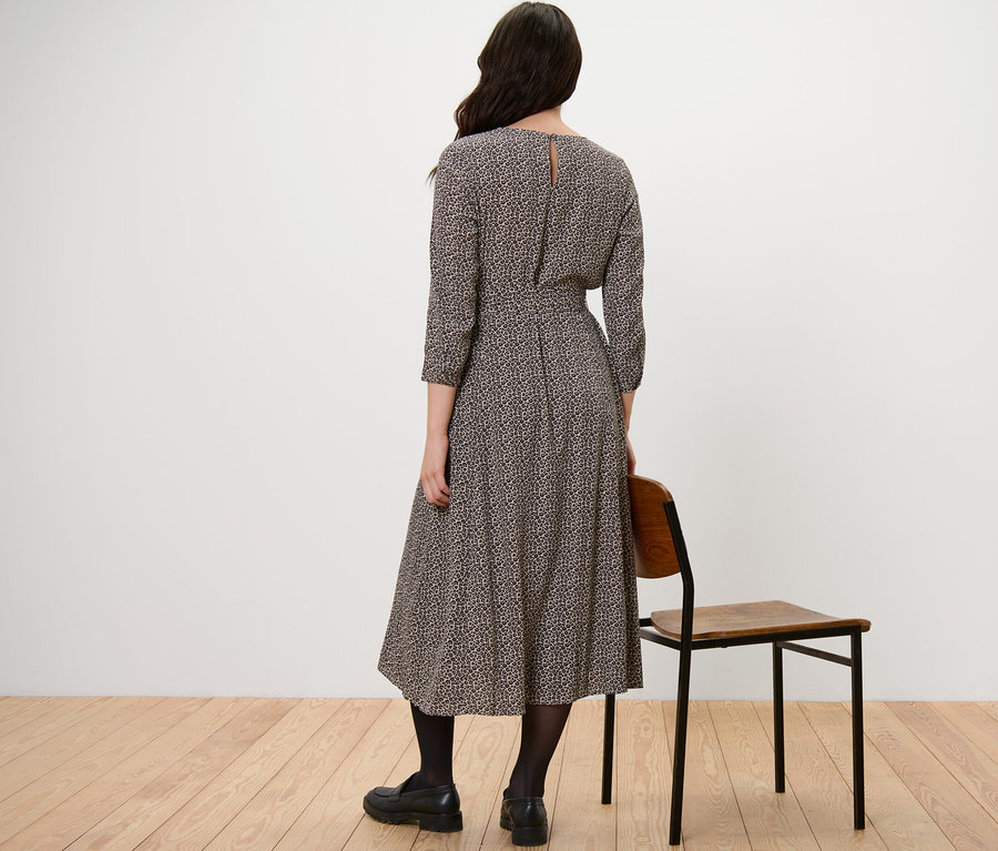 Žena stojí zády k fotoaparátu a má na sobě tkané šaty s potiskem.