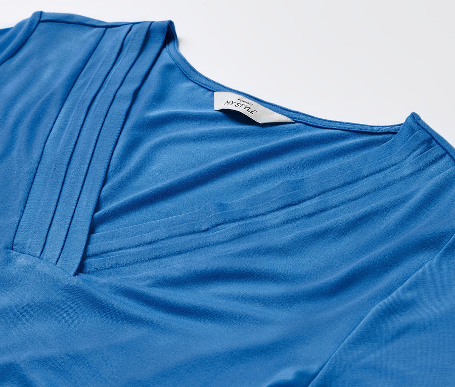 Detail modrého trička s detaily skladů.