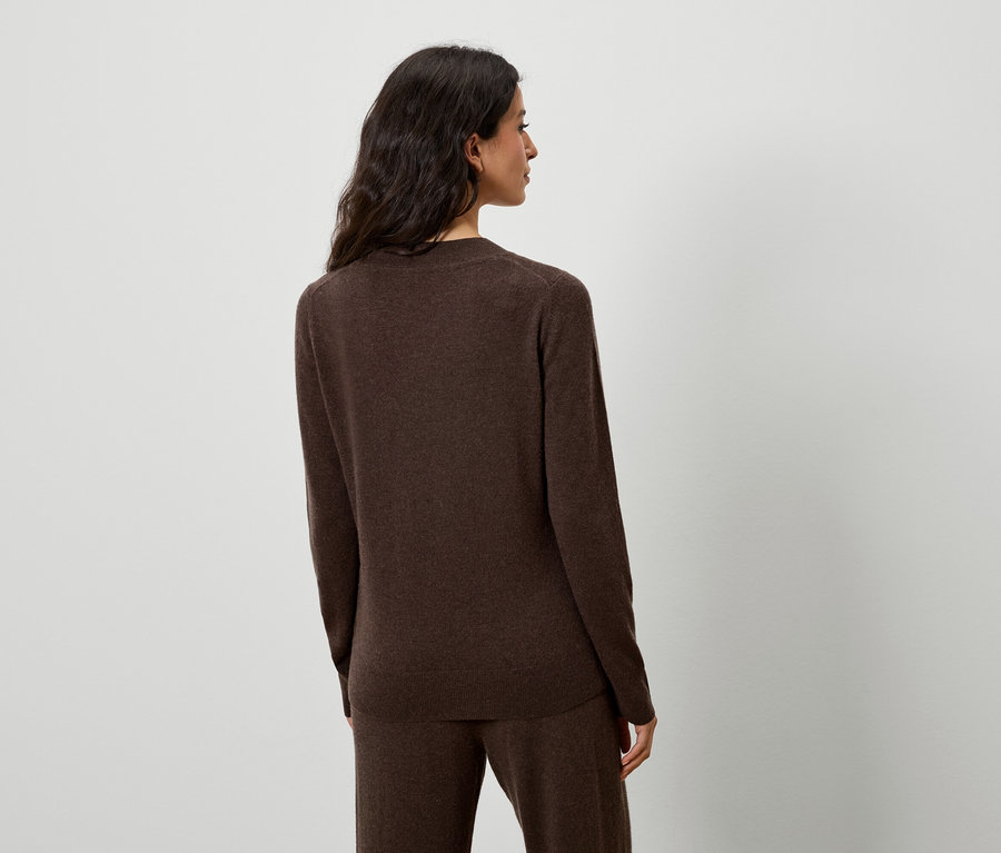 Žena pózuje v hnědém svetru a kalhotách.