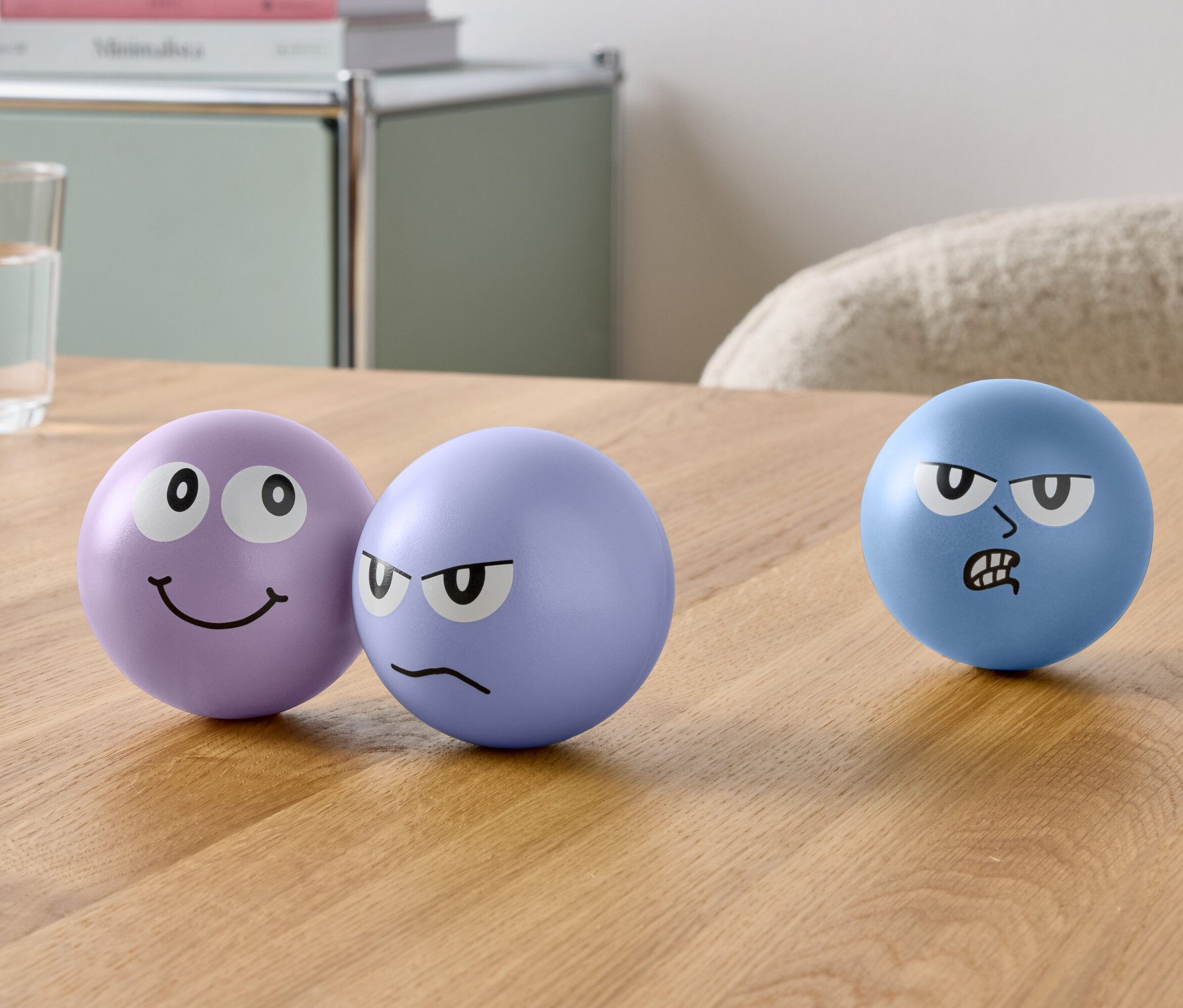 Na stole stojí tři koule s obličeji a sklenice vody.