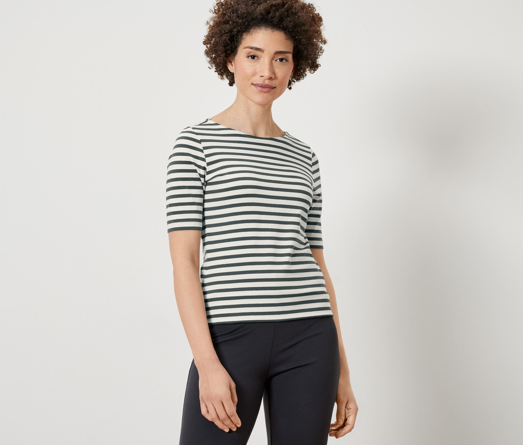 Žena má na sobě tričko s polodlouhým rukávem se zelenými proužky a černé kalhoty.