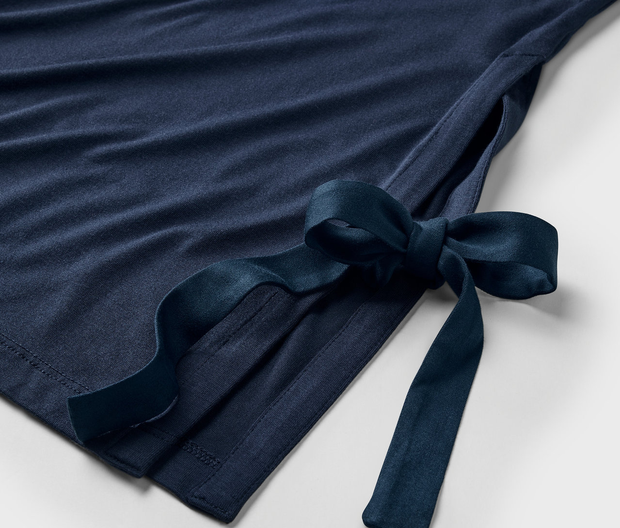 Detail tmavě modrých šatů s mašlí na boku.