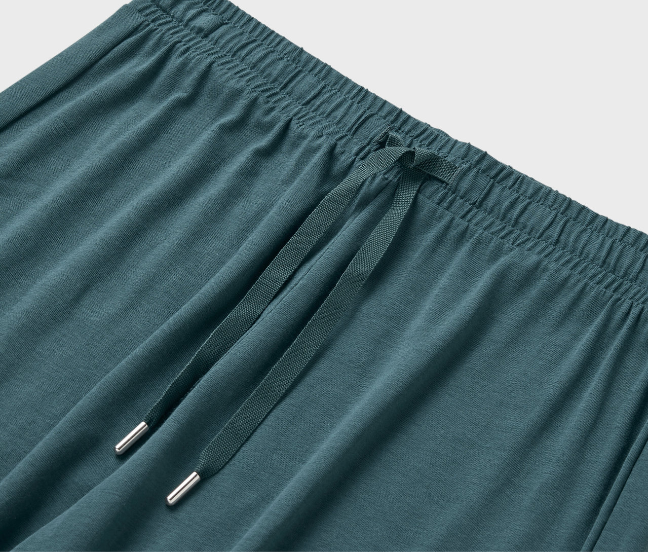 Detailní záběr na elastický pas a stahovací šňůrku zelenomodrých tepláků.
