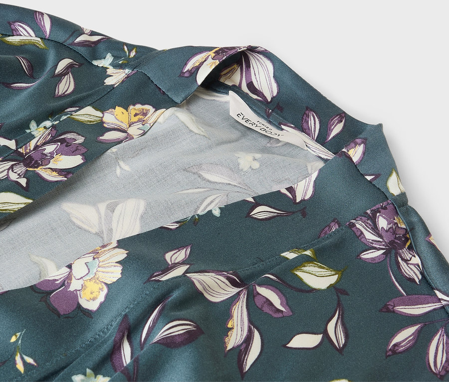 Detail zeleného županu s květinovým vzorem a bílým lemem.