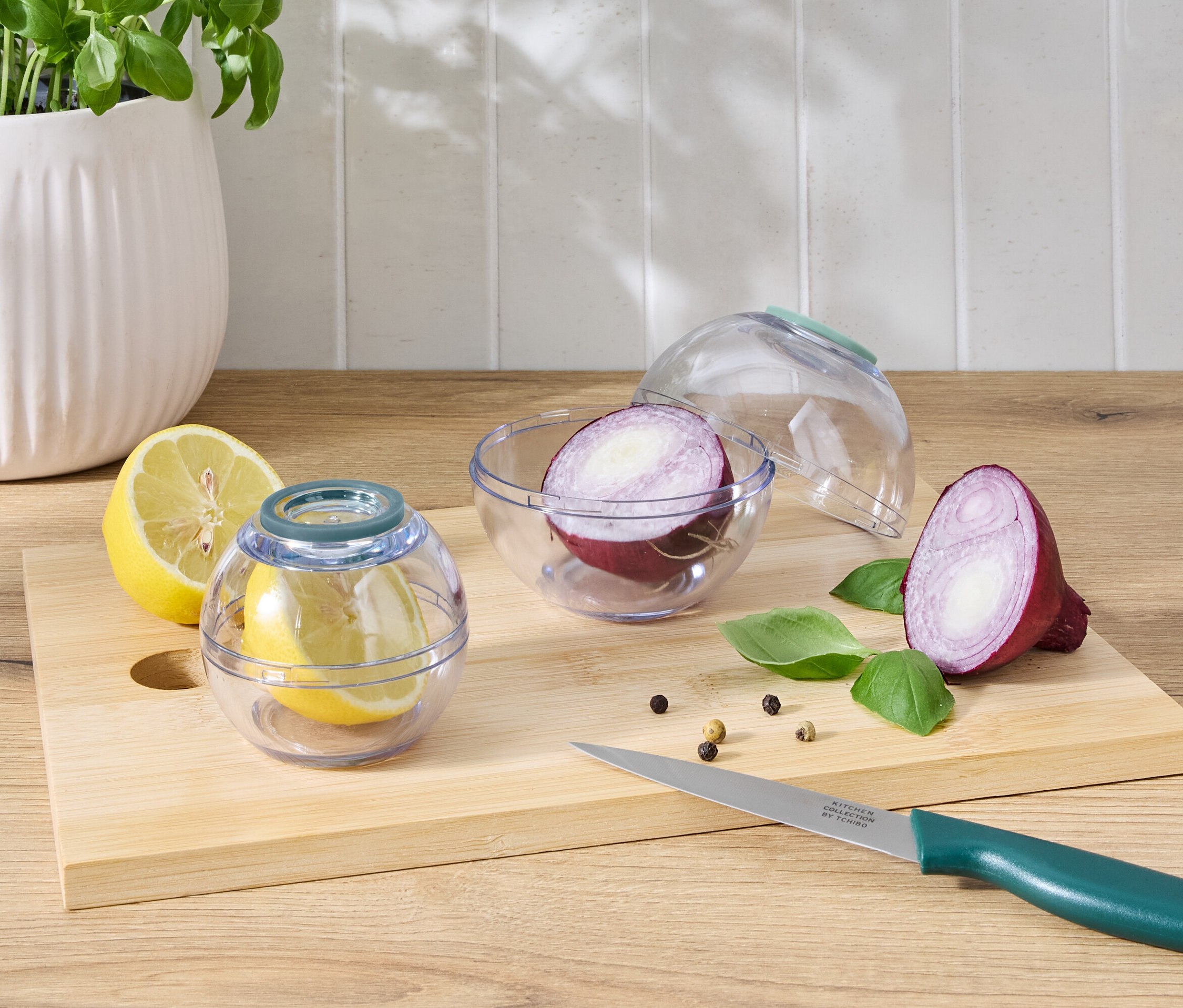 Půlka citronu v průhledné nádobě vedle půlky citronu a půlky červené cibule v průhledné nádobě vedle půlky červené cibule na prkénku s nožem.