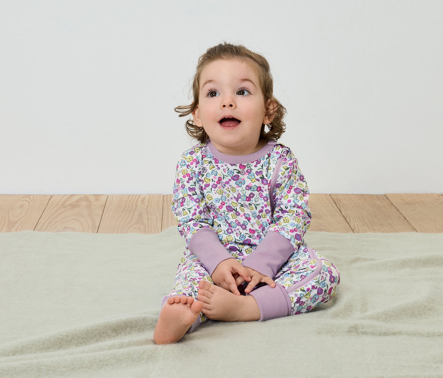 Dítě sedí na dece a má na sobě pyžamo s květinovým vzorem.