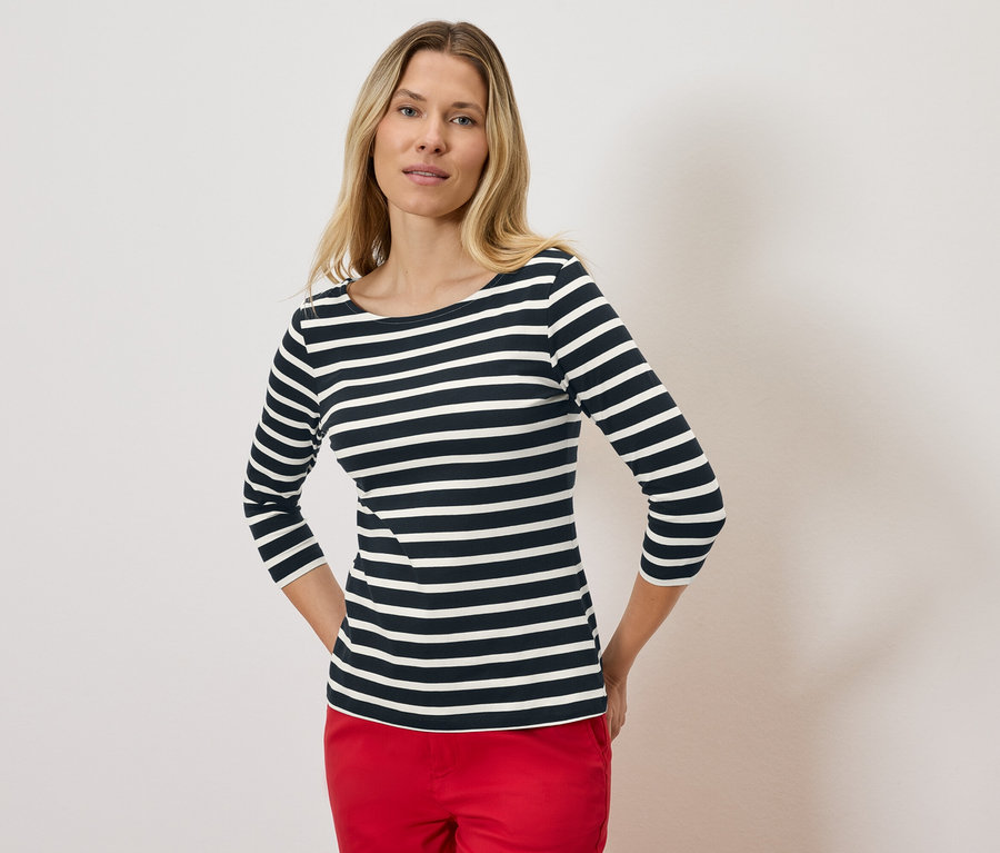 Blondýna v pruhovaném tričku s tříčtvrtečním rukávem a červených kalhotách.