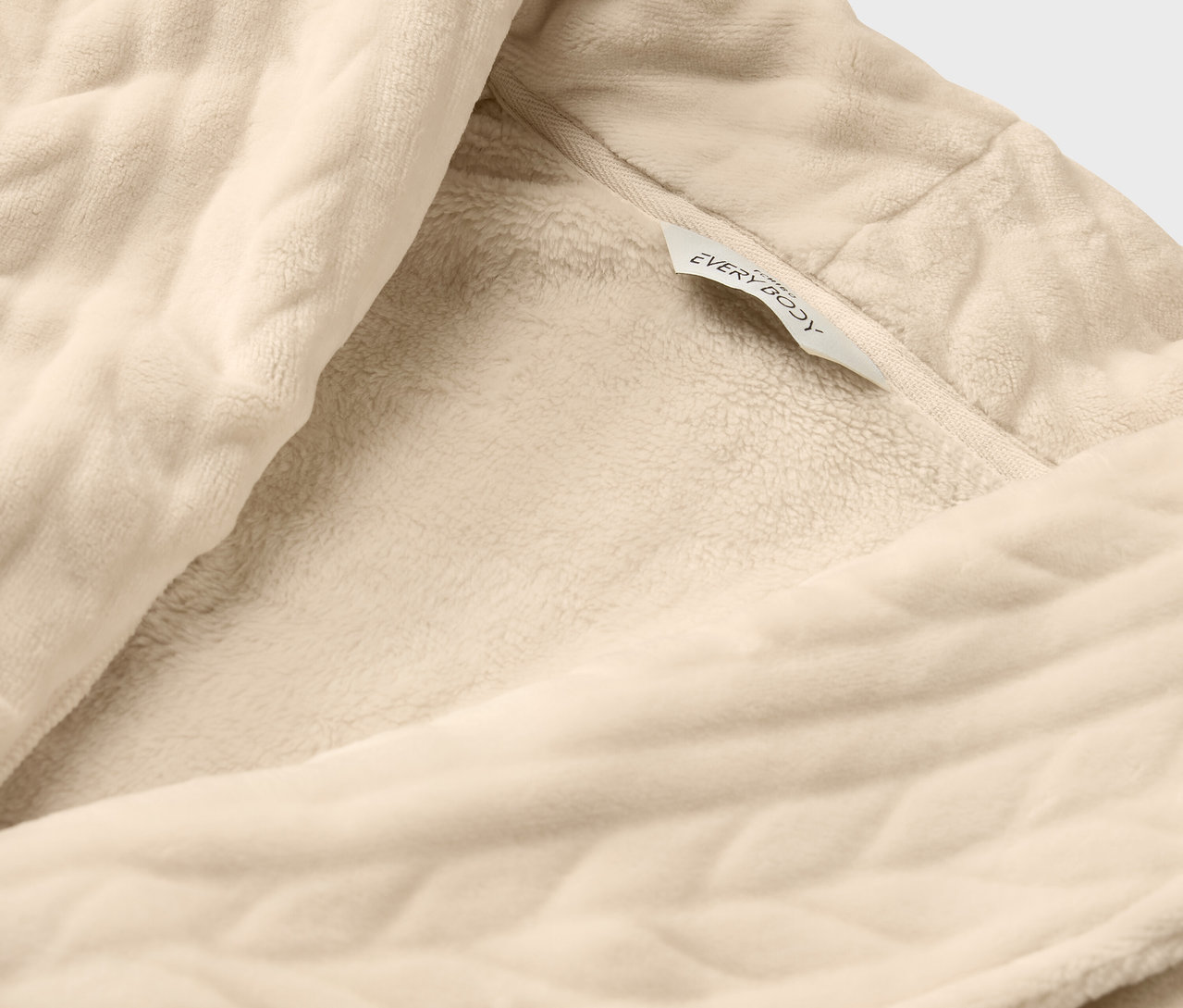 Detail krémového županu s texturou a štítkem "everybody".