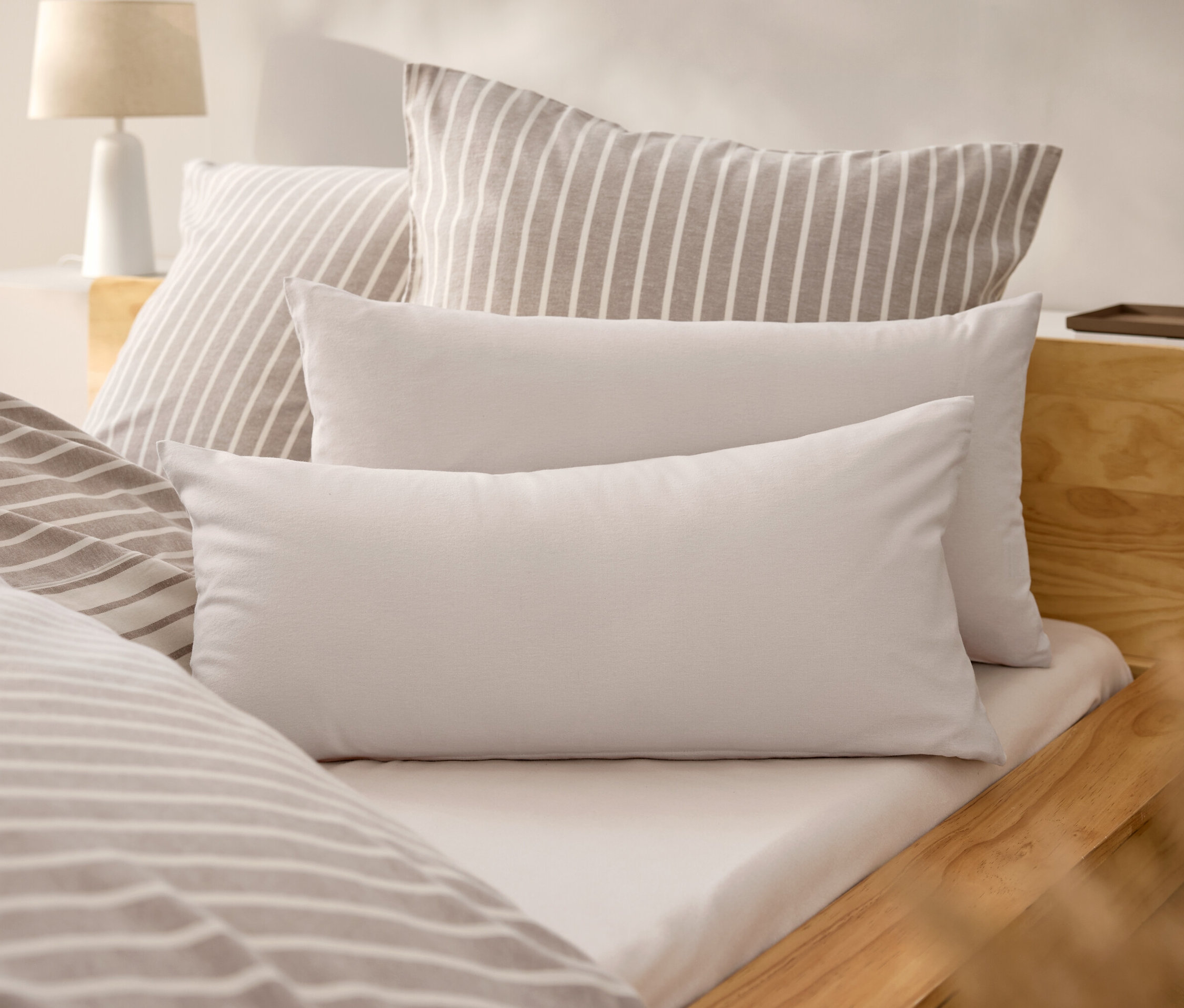 Postel s bílým prostěradlem a polštáři s béžovými pruhy.