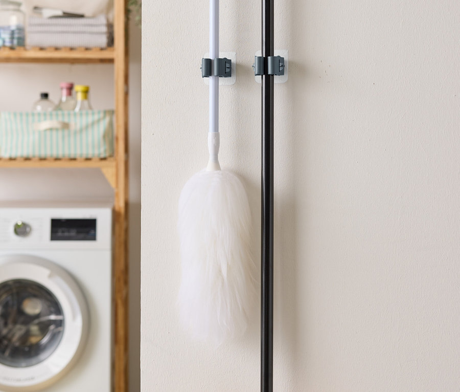Na zdi visí prachovka a smeták, v pozadí je pračka a regál.