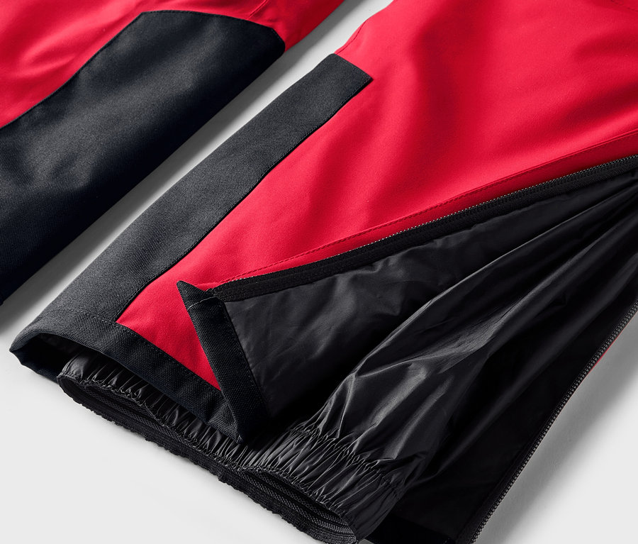 Detail červeno-černých kalhot s rozepnutým zipem na nohavici.