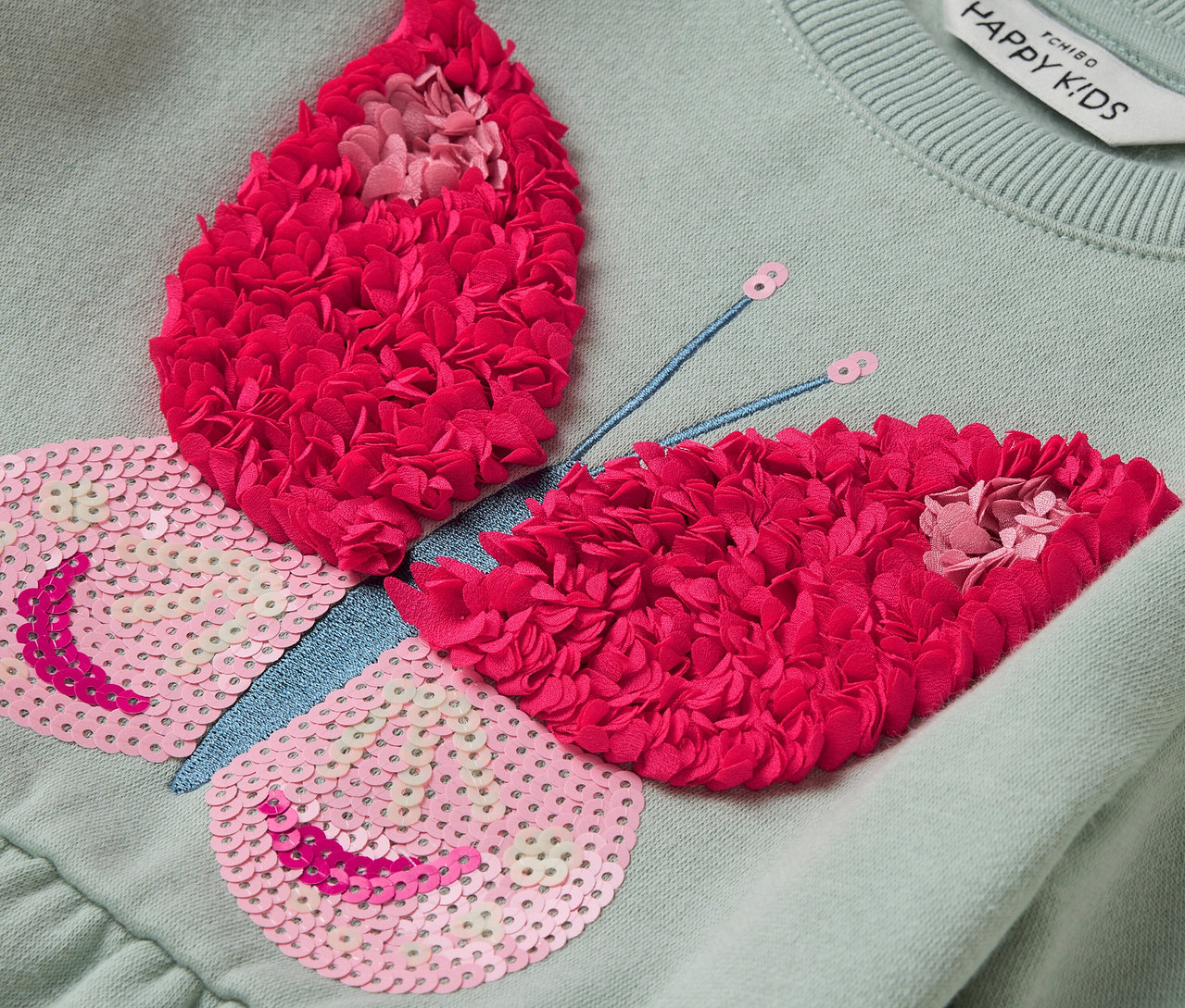 Světle zelené šaty s aplikací motýla s růžovými flitry a červenými květy.