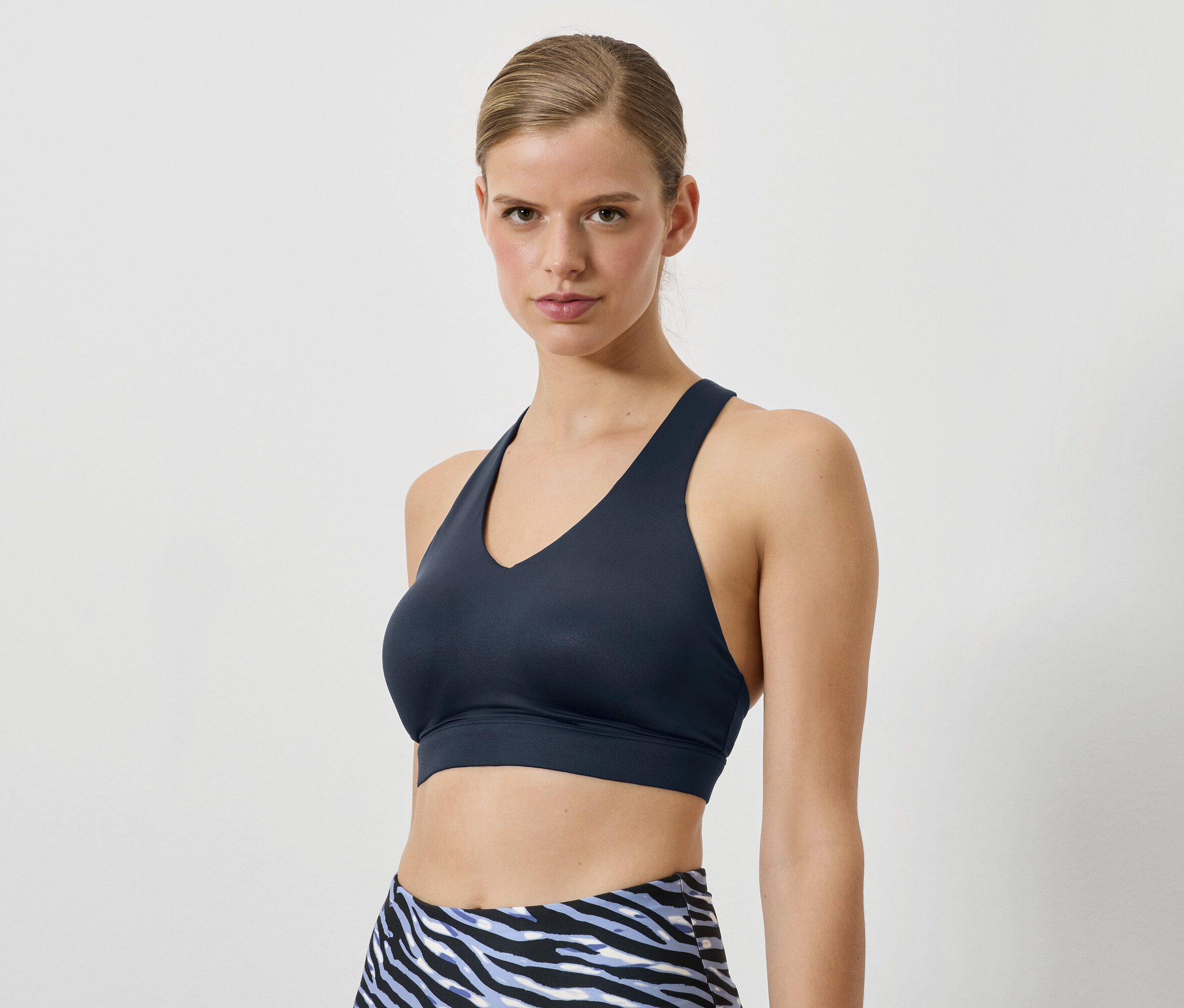 Žena má na sobě tmavě modrou sportovní podprsenku a legíny se zvířecím vzorem.