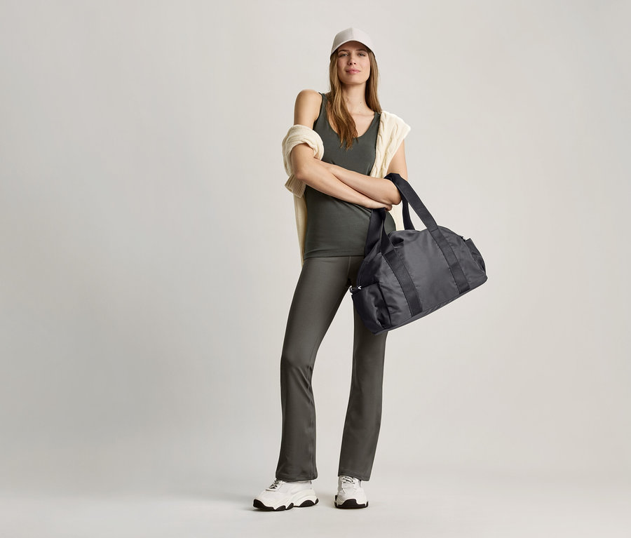 Žena pózuje v olivově zeleném topu a černé sportovní tašce.