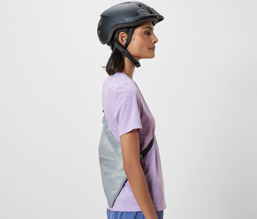 Boční pohled na ženu s cyklistickou helmou. Přes rameno má přehozenou nákupní tašku na kolo.