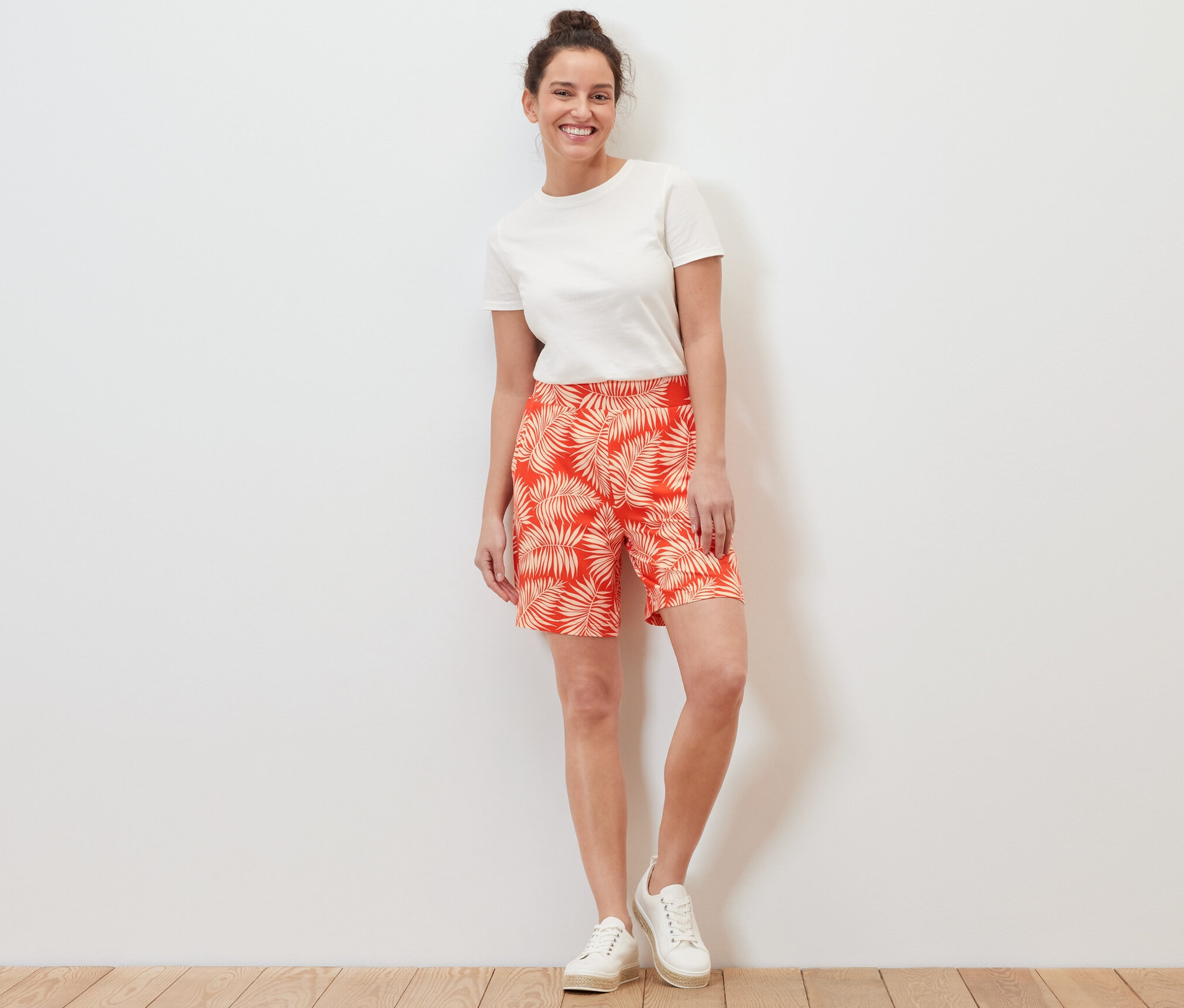 Žena stojí a má na sobě džínové šortky s potiskem a bílé tričko.