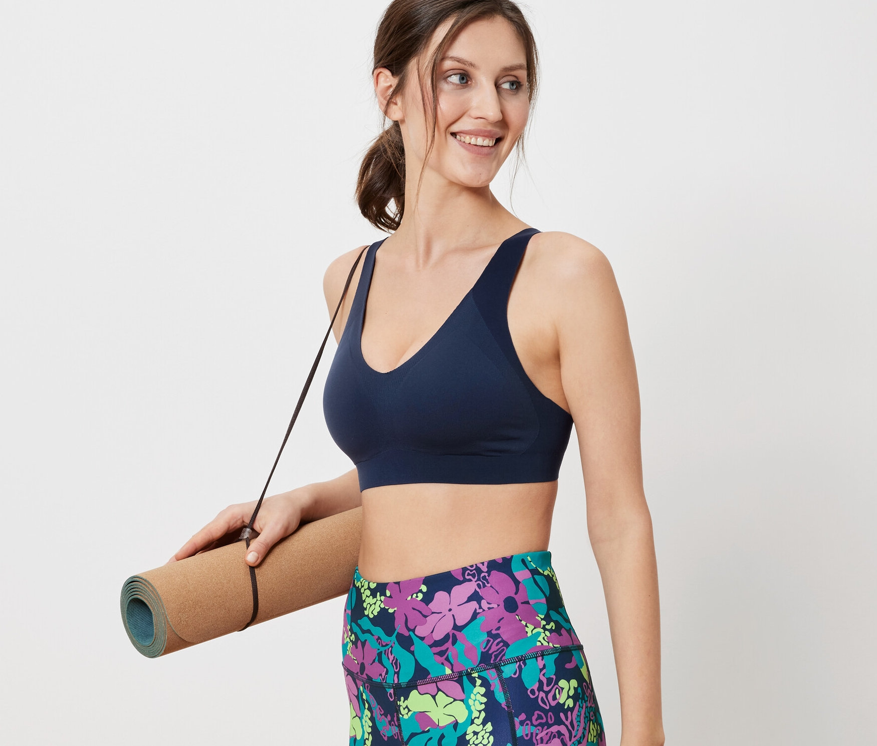 Žena drží podložku na cvičení a má na sobě sportovní podprsenku.